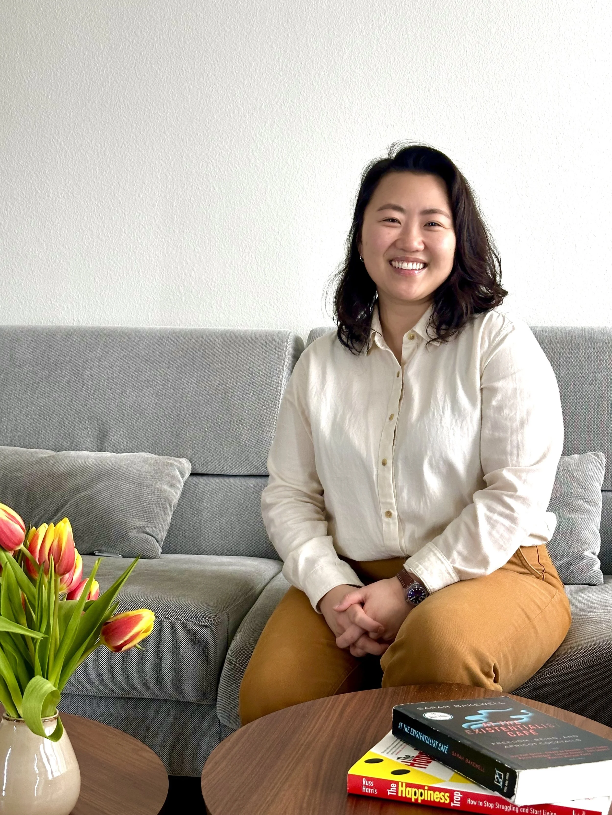 Asian woman sitting on a grey couch with red and yellow tulips on the coffee table in the foreground