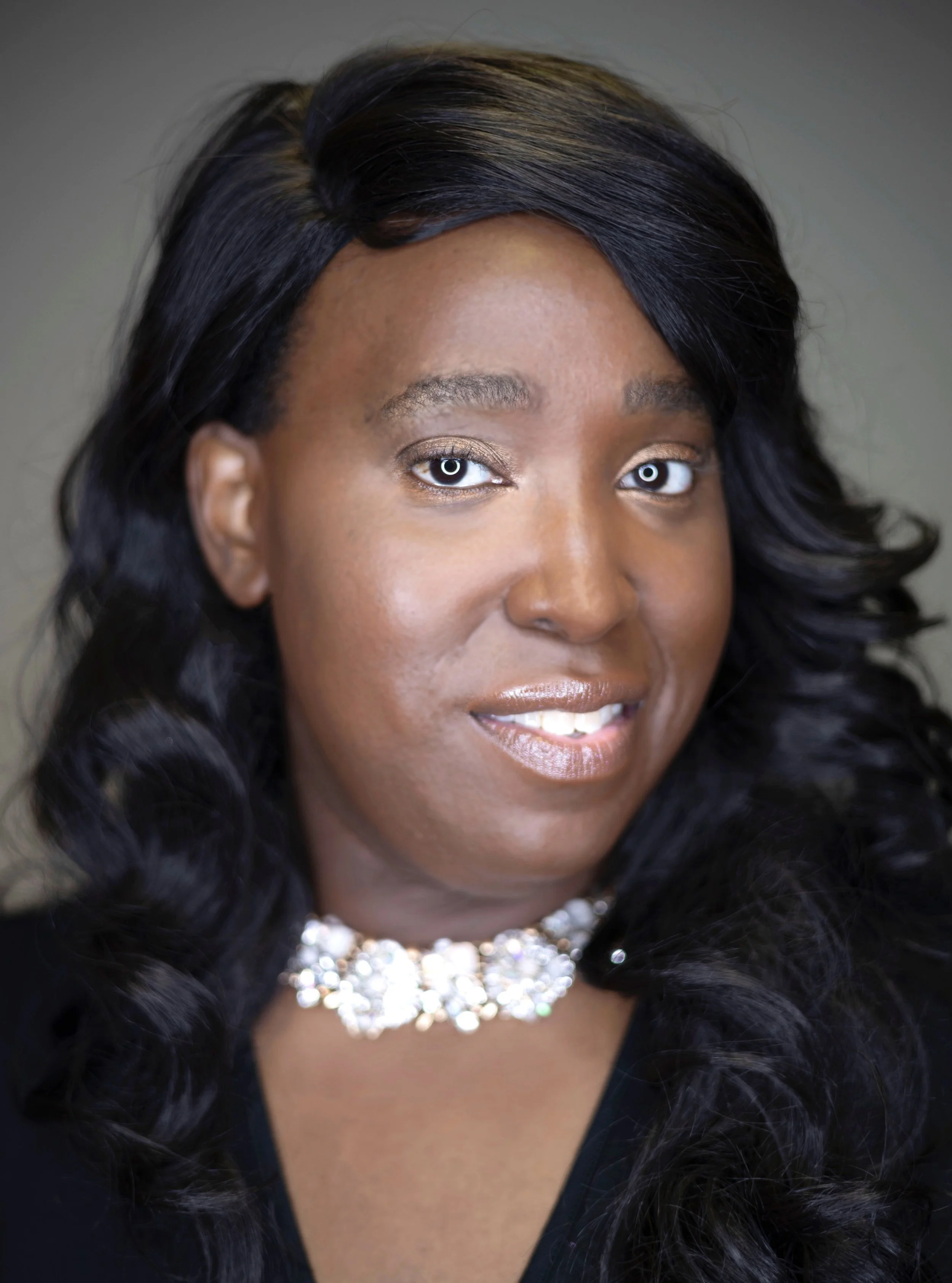 Portrait of a woman with dark, wavy hair and a sparkling necklace, smiling softly.