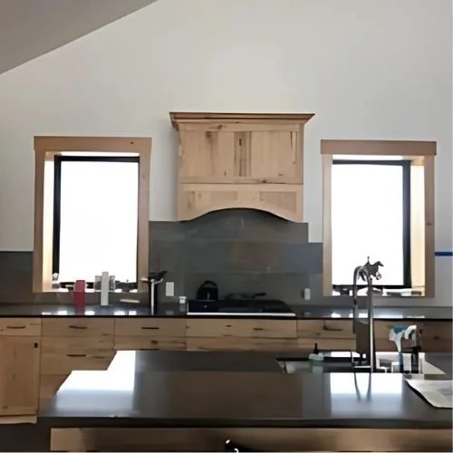 Kitchen with two windows, wooden cabinetry, a central black stove, and a countertop with a faucet and various items.