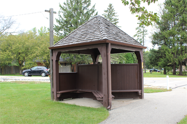 The Bell Road Bus Stop Shelter at the southwest corner of N. Lake Drive and Bell Road in Fox Point, built in 1940 and featuring a rustic wood-shingled, hipped roof design.