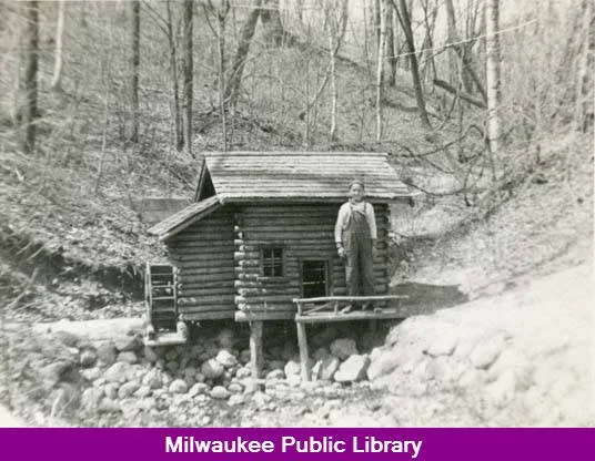 This photo shows a small log cabin in Doctors Park. A boy, identified only as Kenny, stands on the porch and is as tall as the roof of the cabin.