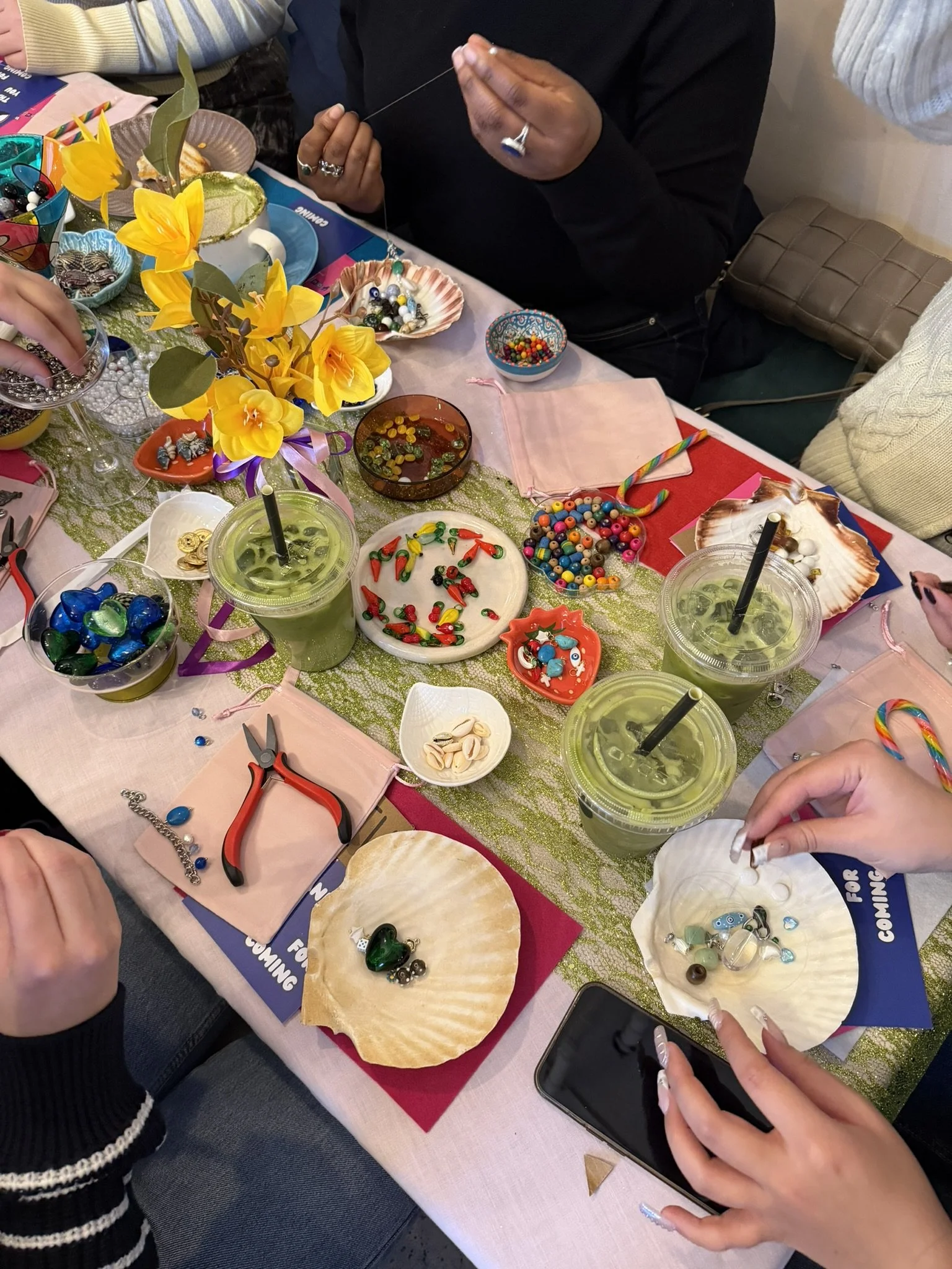 Hands creating jewelry with various beads and jewelry-making supplies on a decorated table.