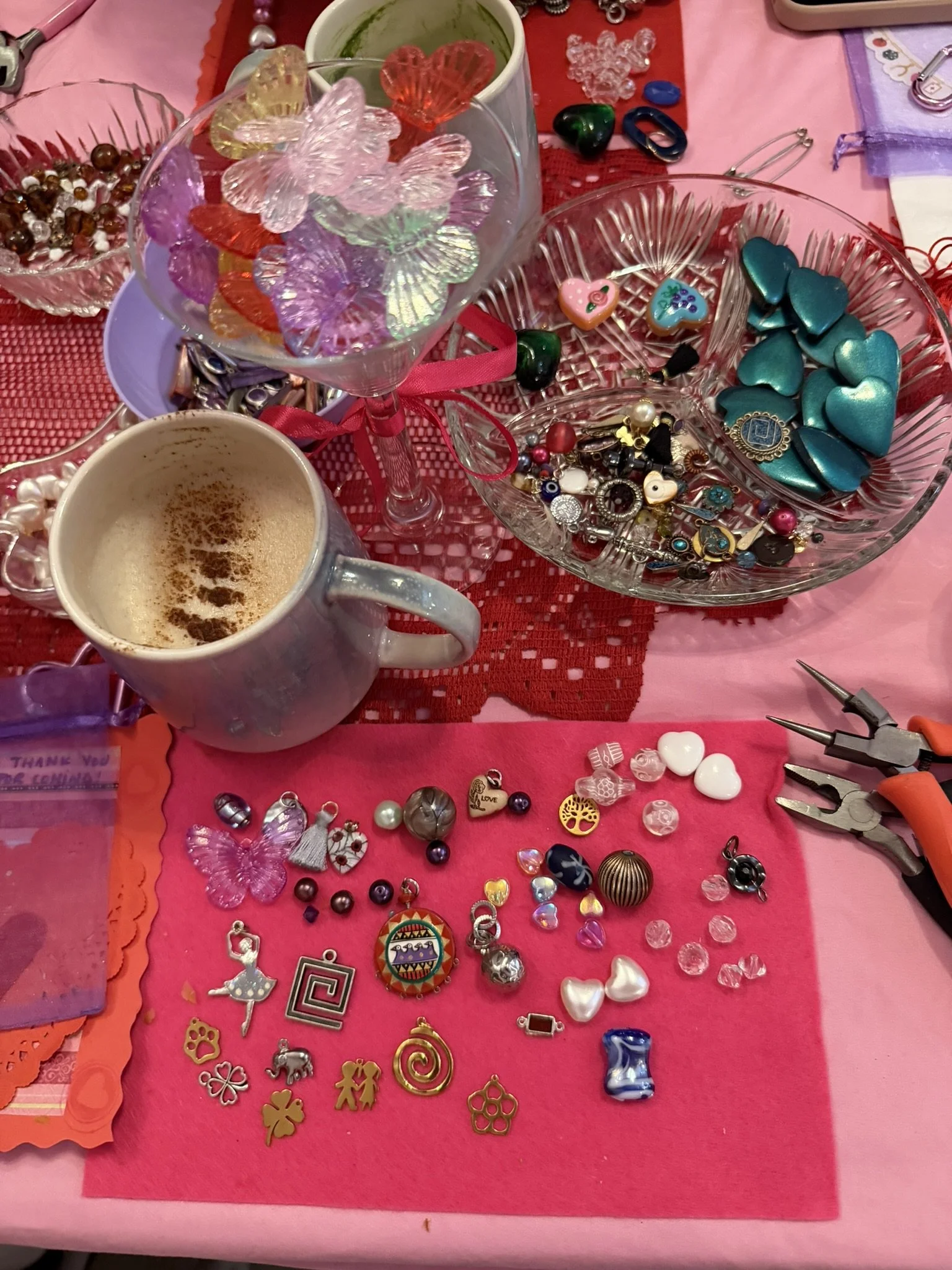 A table covered with various colorful jewelry and trinkets, including heart-shaped, butterfly-shaped, and other decorative items, with some jewelry in bowls and scattered on pink and red fabric.