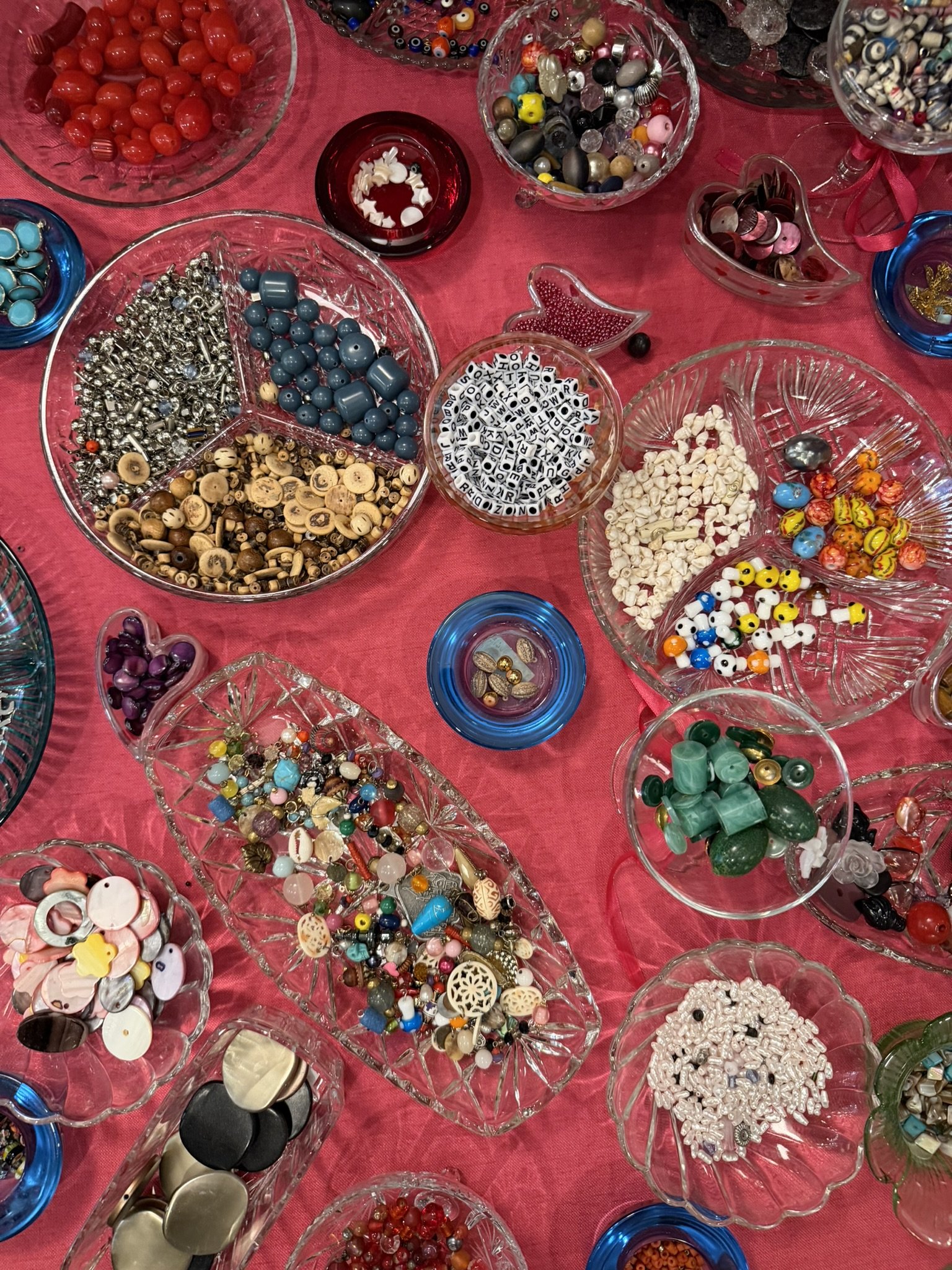 Various bowls and containers filled with different buttons, beads, and craft supplies on a red tablecloth.