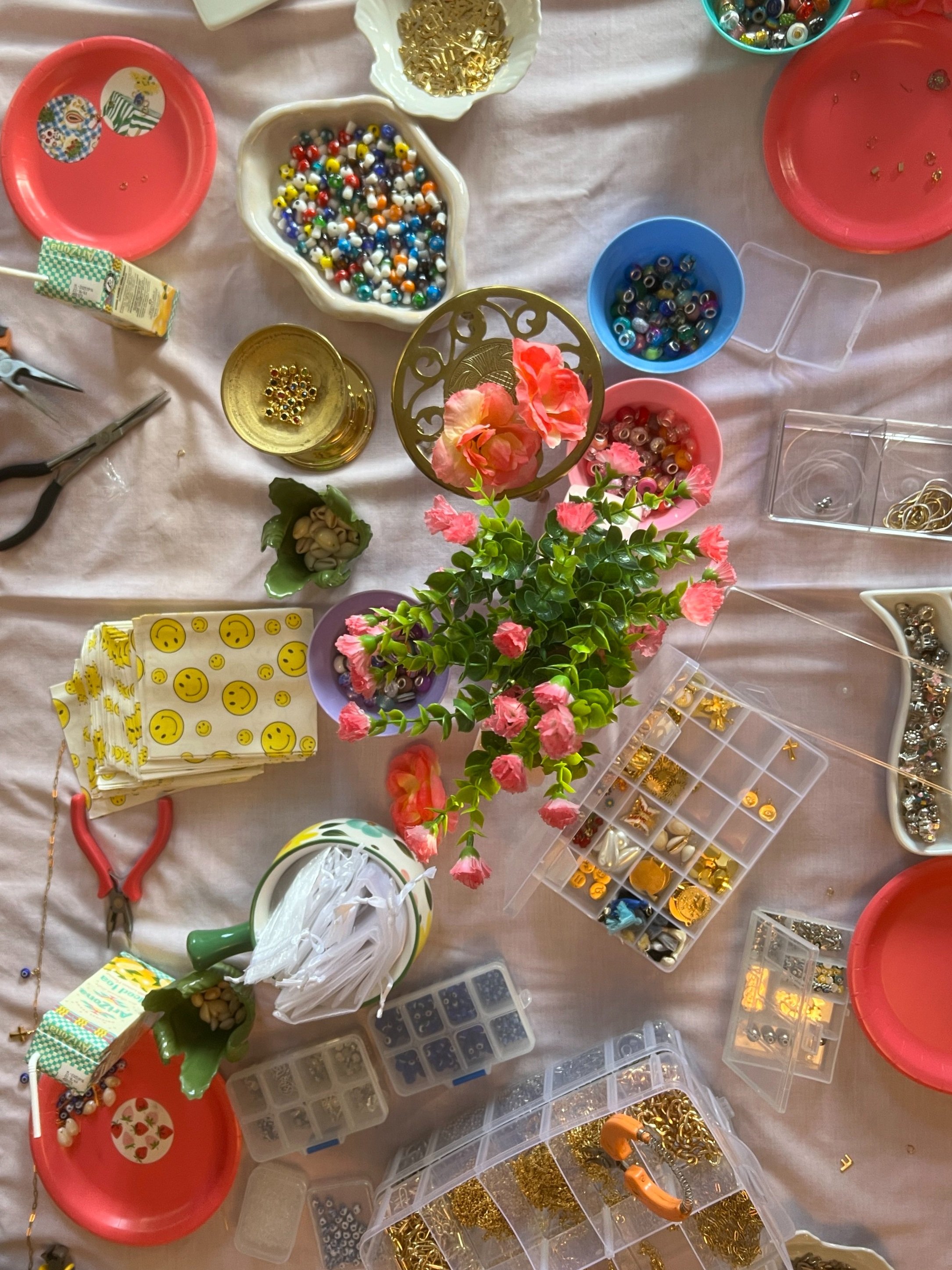 A table with various craft supplies including colorful beads, containers, pliers, decorative flowers, and handmade stickers.
