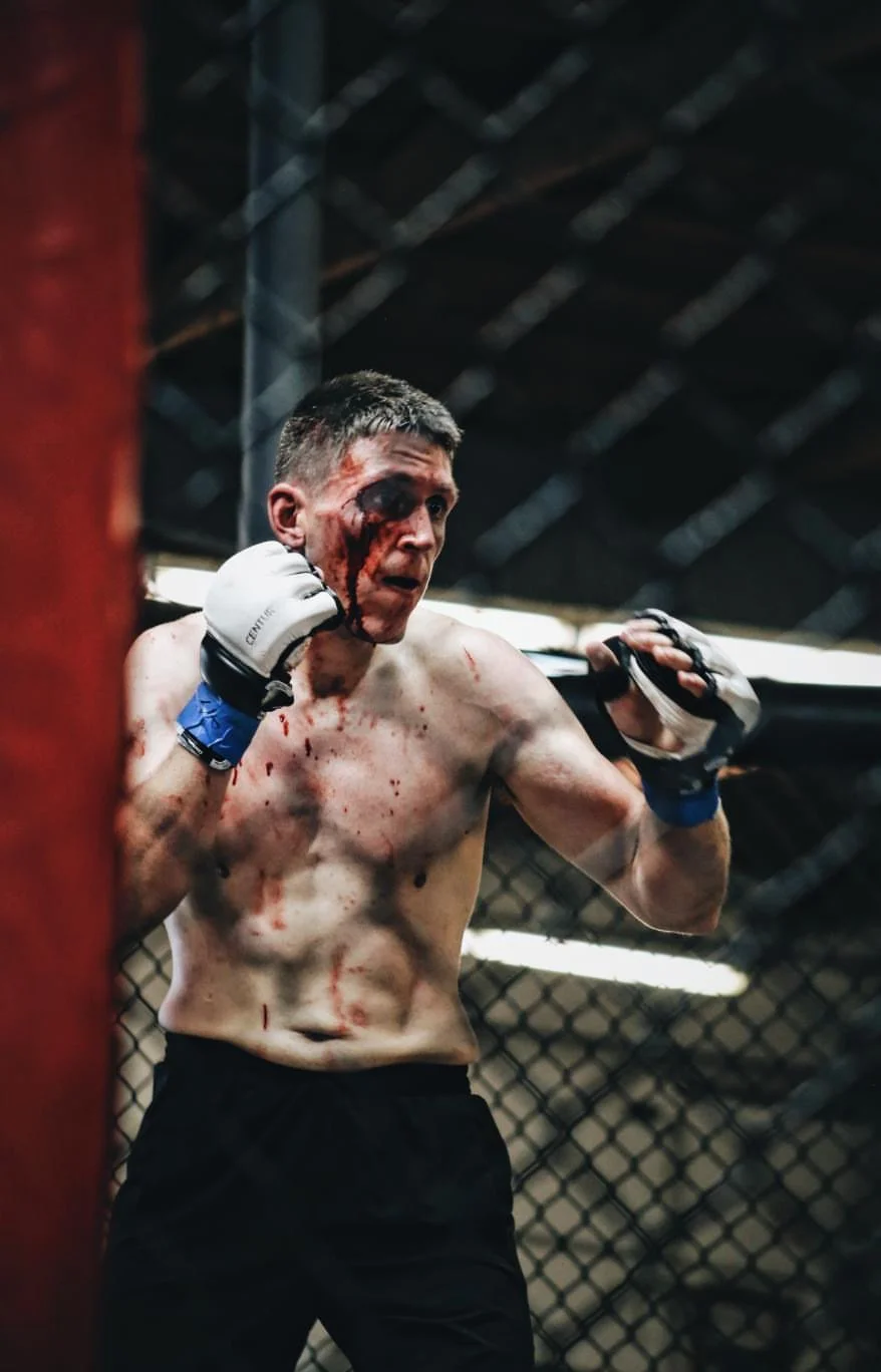 A bruised and bloodied male mixed martial arts fighter with short dark hair training in an MMA cage.