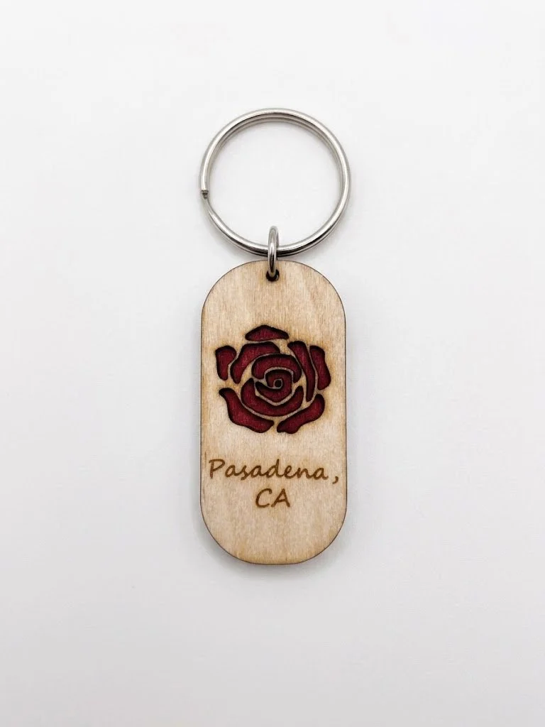 A wooden keychain with a red rose design and the words 'Pasadena, CA' engraved.