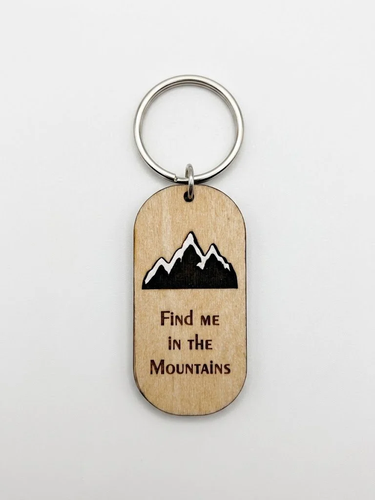 Wooden keychain with an engraved mountain range and the words "Find me in the Mountains".
