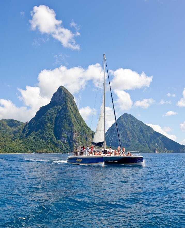 A sailboat on the water with green mountainous islands in the background under a partly cloudy blue sky.
