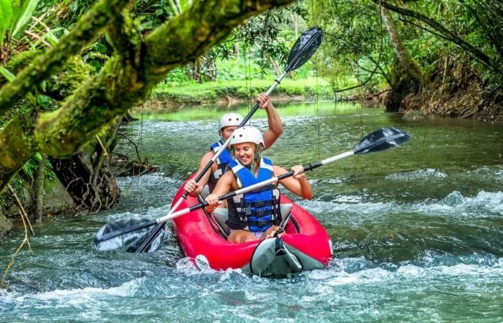Two people in a red kayak paddling through a river surrounded by lush green trees.