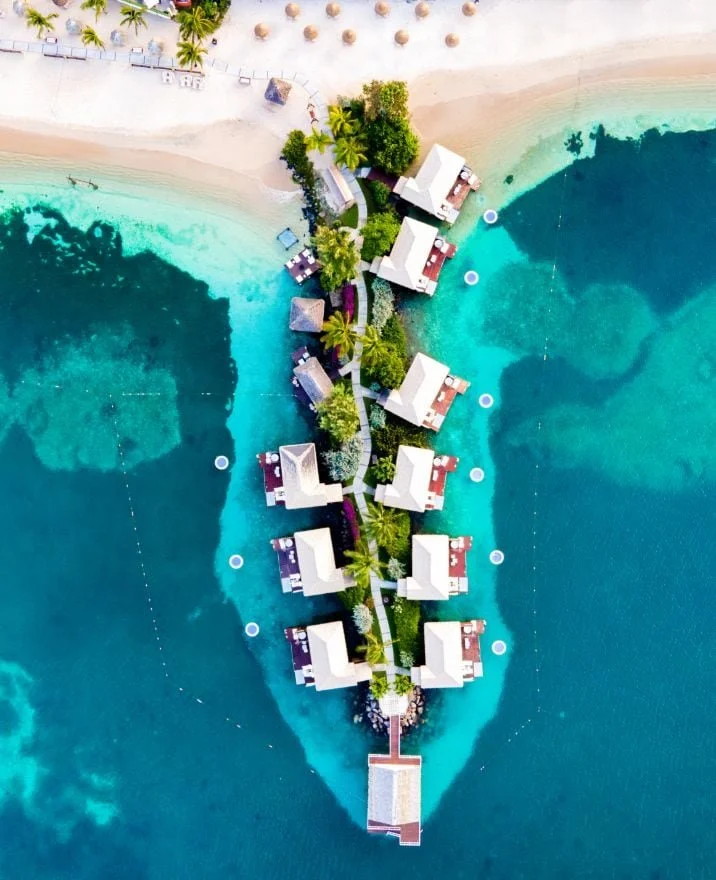 Aerial view of overwater bungalows on a tropical island with clear turquoise water and white sandy beach.