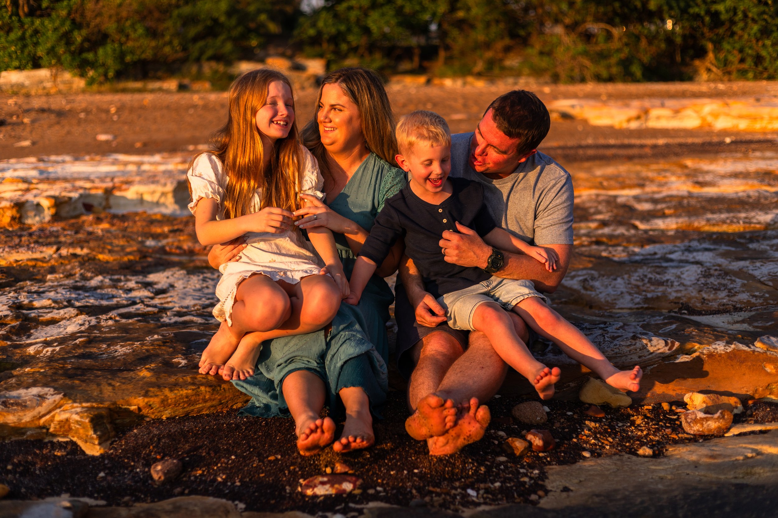 Family of five smiling outdoors with rocky background during sunset.
