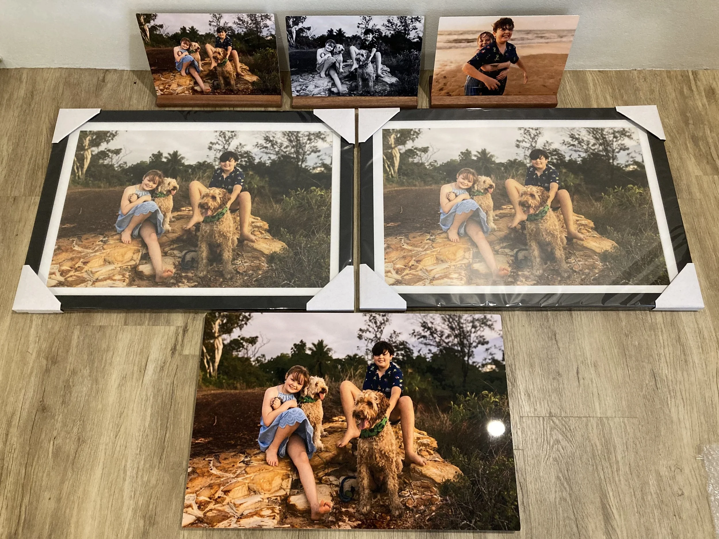 Various printed and framed photographs of two children and a dog placed on a wooden surface.