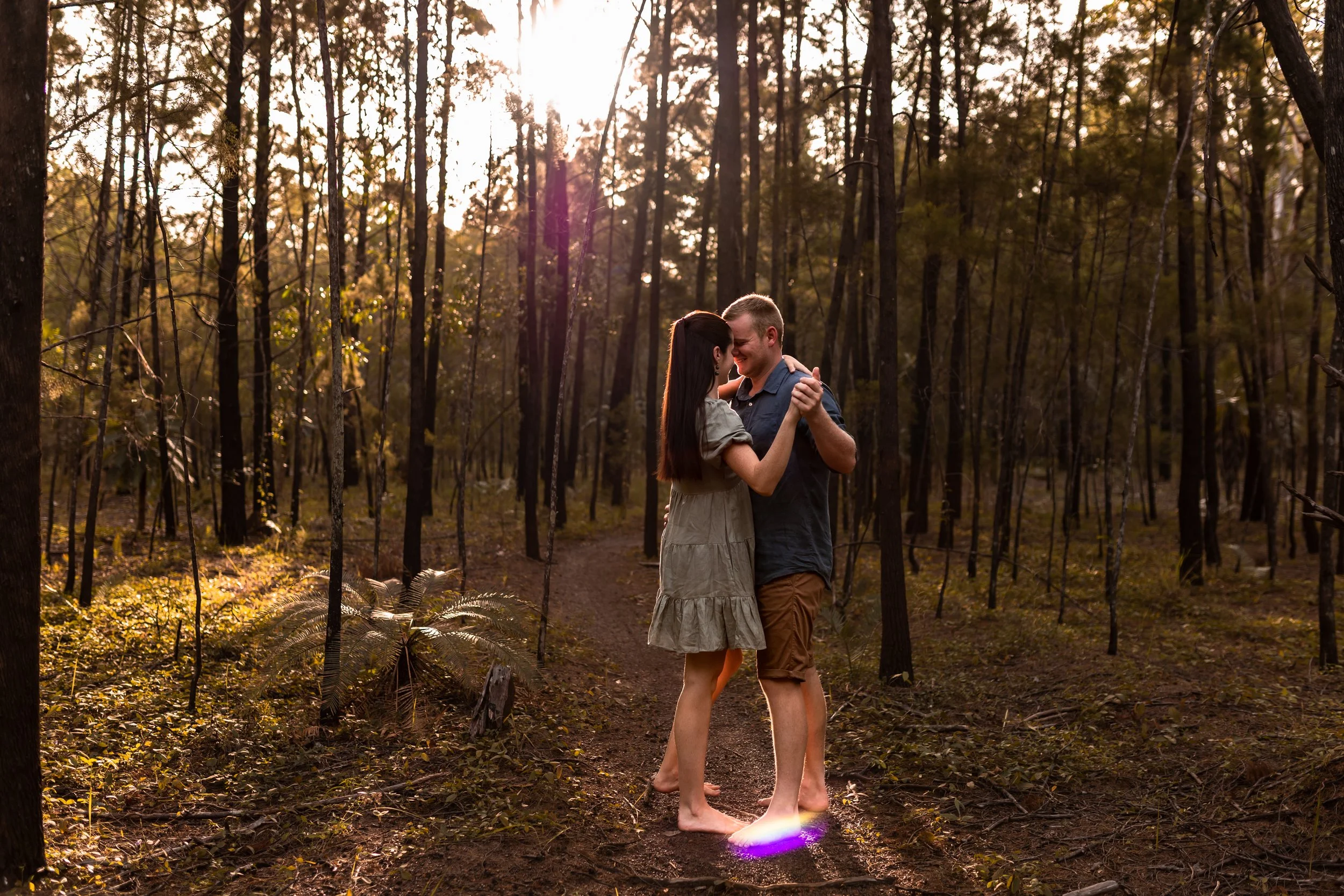 A couple dancing barefoot on a trail in a forest at sunset.