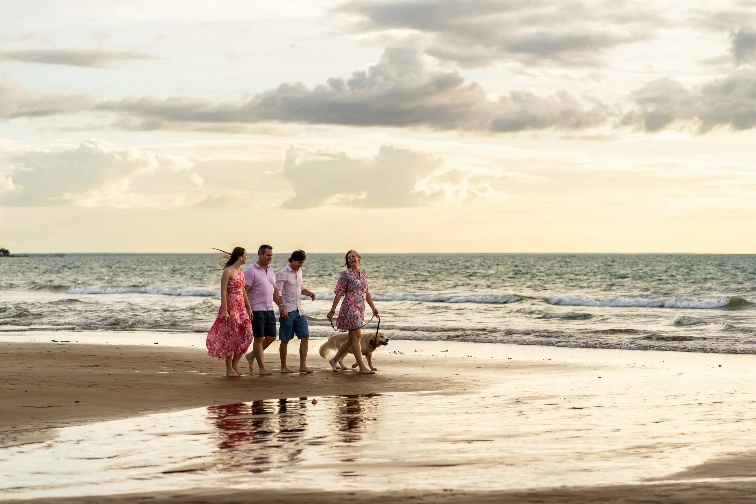 A family of five celebrating outdoors at sunset, with three members on a black vehicle's tailgate, holding drinks and smiling. Two boys are standing on either side of the vehicle, one girl sits on the tailgate, and a man stands next to them, also smiling.