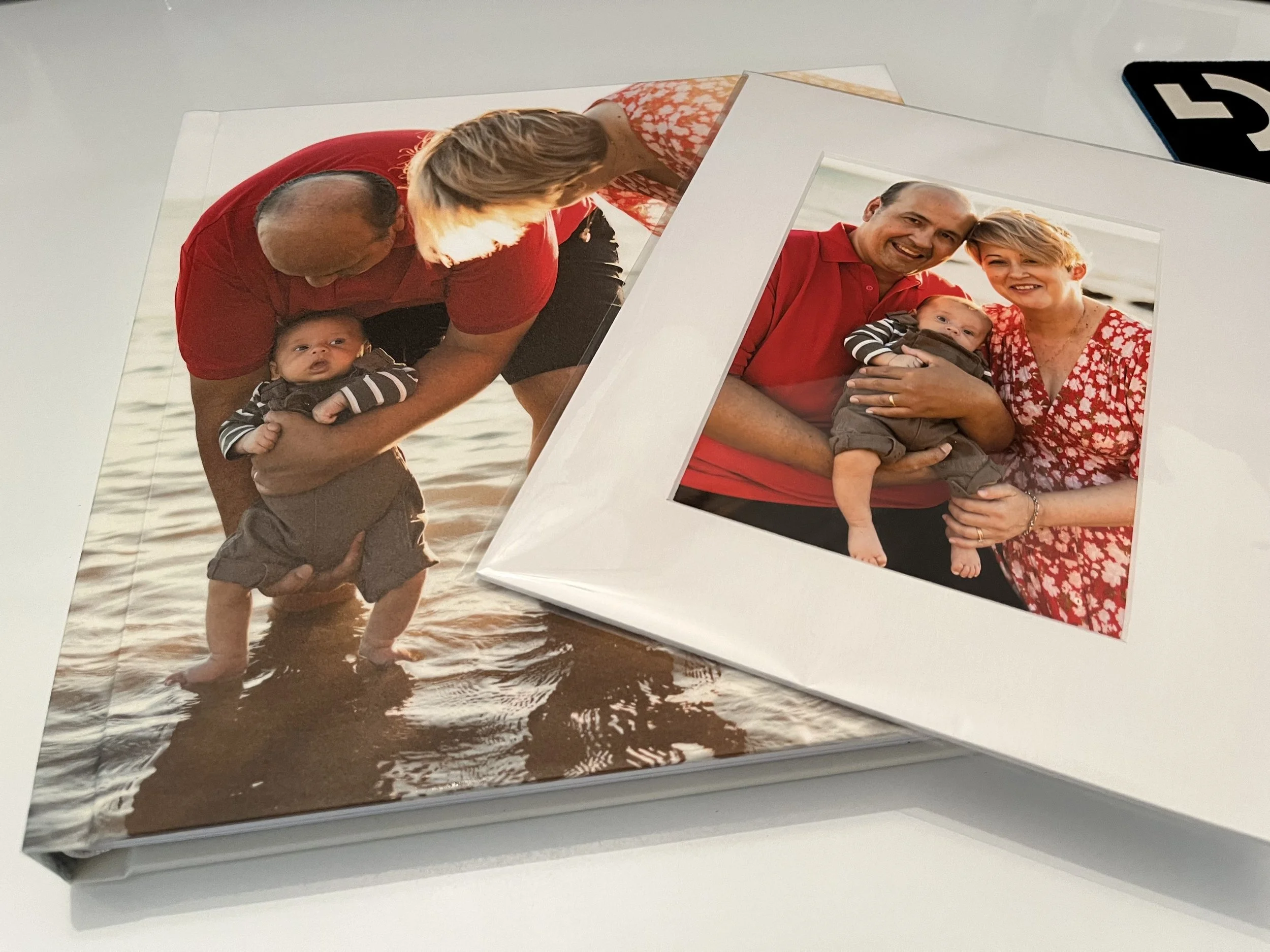 Two photo albums, one open with a picture of a family on the beach, and the other with a family portrait, both featuring a man, woman, and a baby boy, all smiling and wearing red clothing.