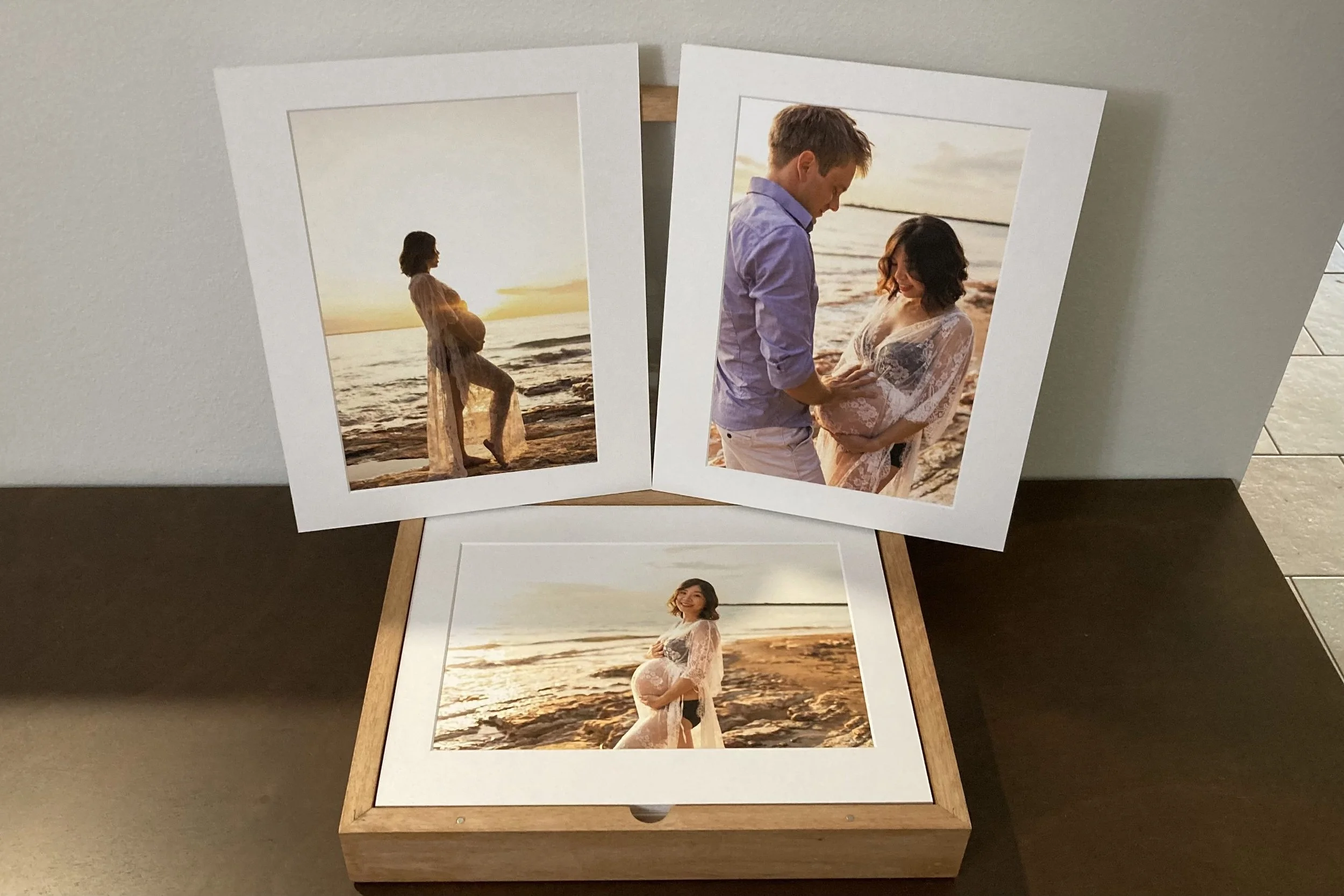 Set of three framed and unframed photographs of a pregnant woman on the beach during sunset, posing alone and with a man, with waves and sand in the background.