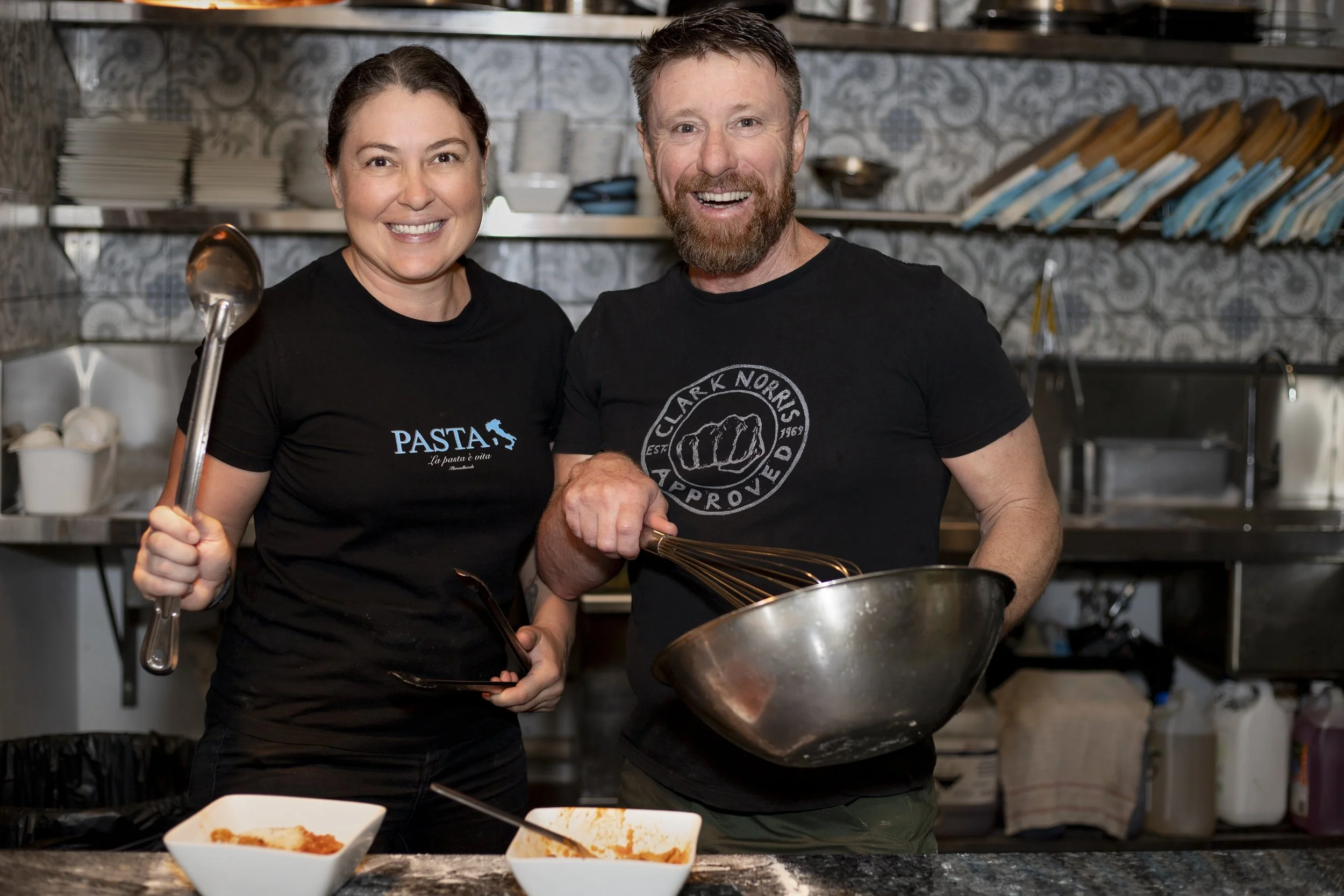 Smiling woman and man in a kitchen, cooking together with bowls and utensils, showing happiness.