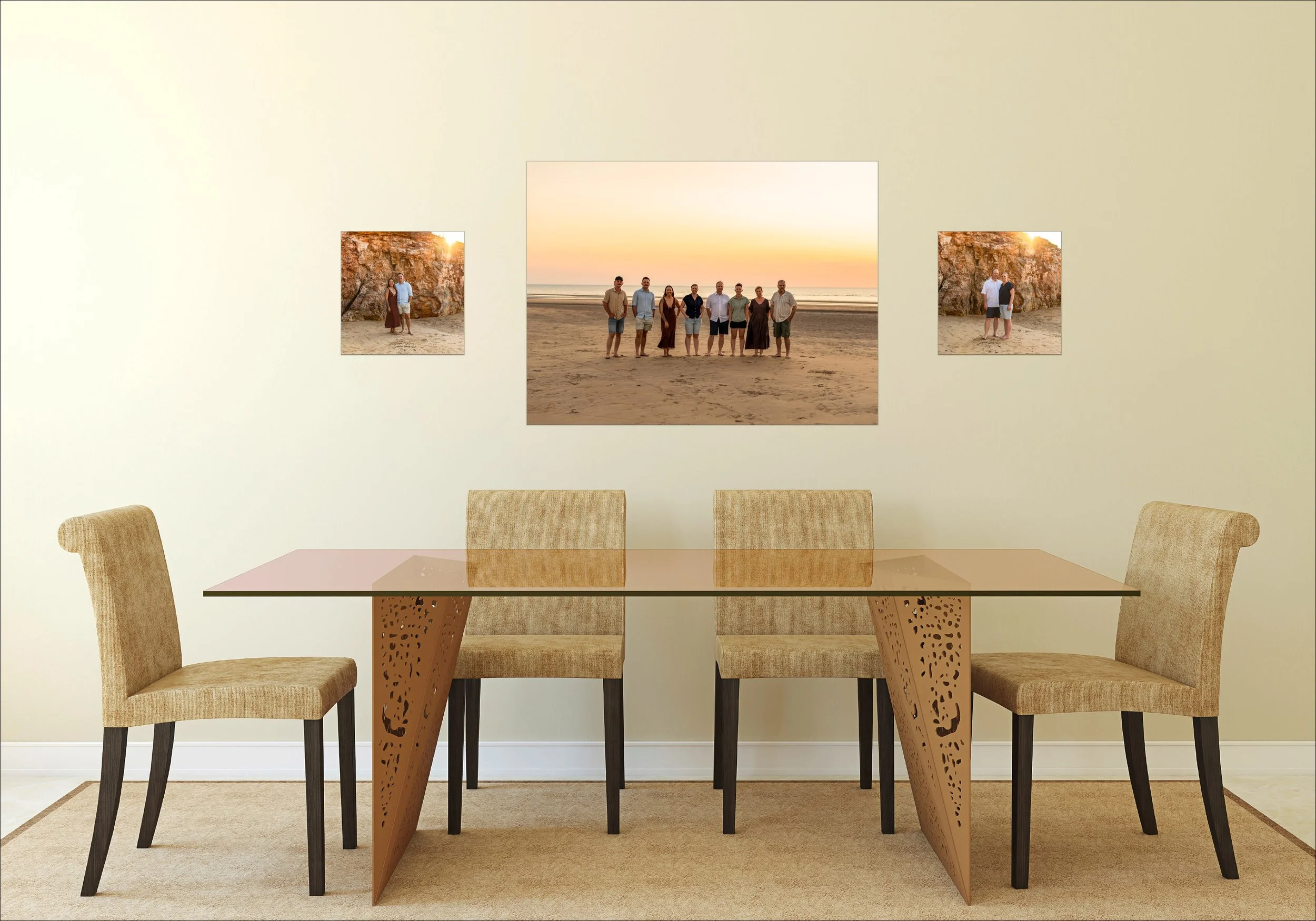 A dining room with a glass-top table and four beige upholstered chairs with black legs, set on a beige rug. The light-colored wall behind features three framed photographs of a group of people at the beach during sunset, with the central photo showin