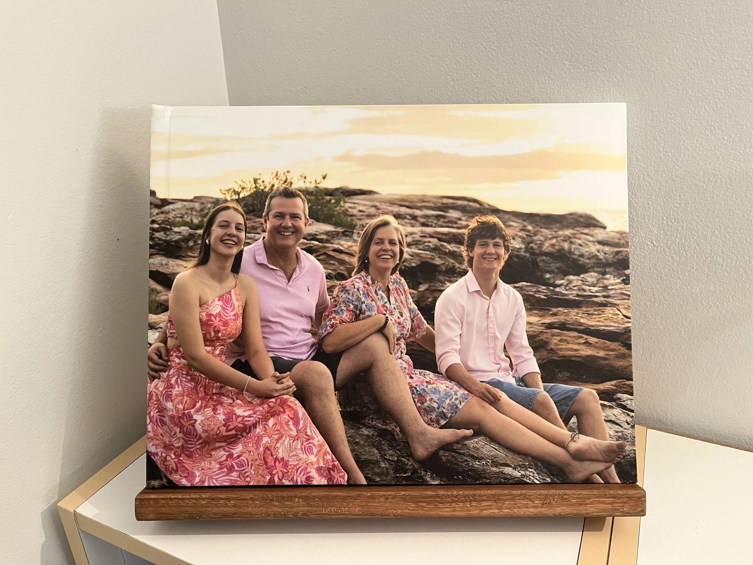 Family of four sitting on rocks at sunset, smiling, outdoors