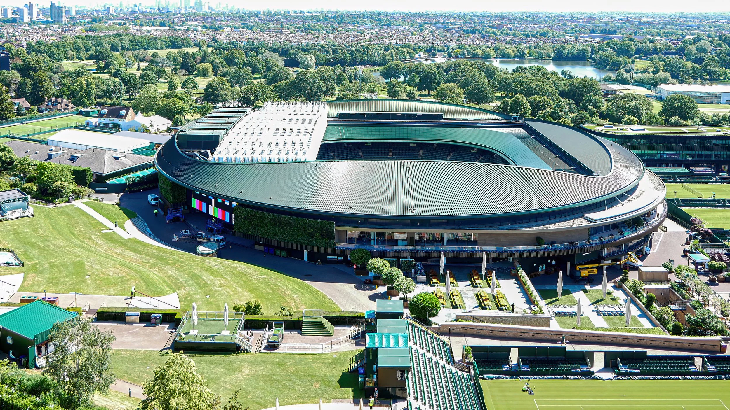 Aerial view of Wimbledon tennis complex with iconic tennis courts and main stadium in a lush green landscape.