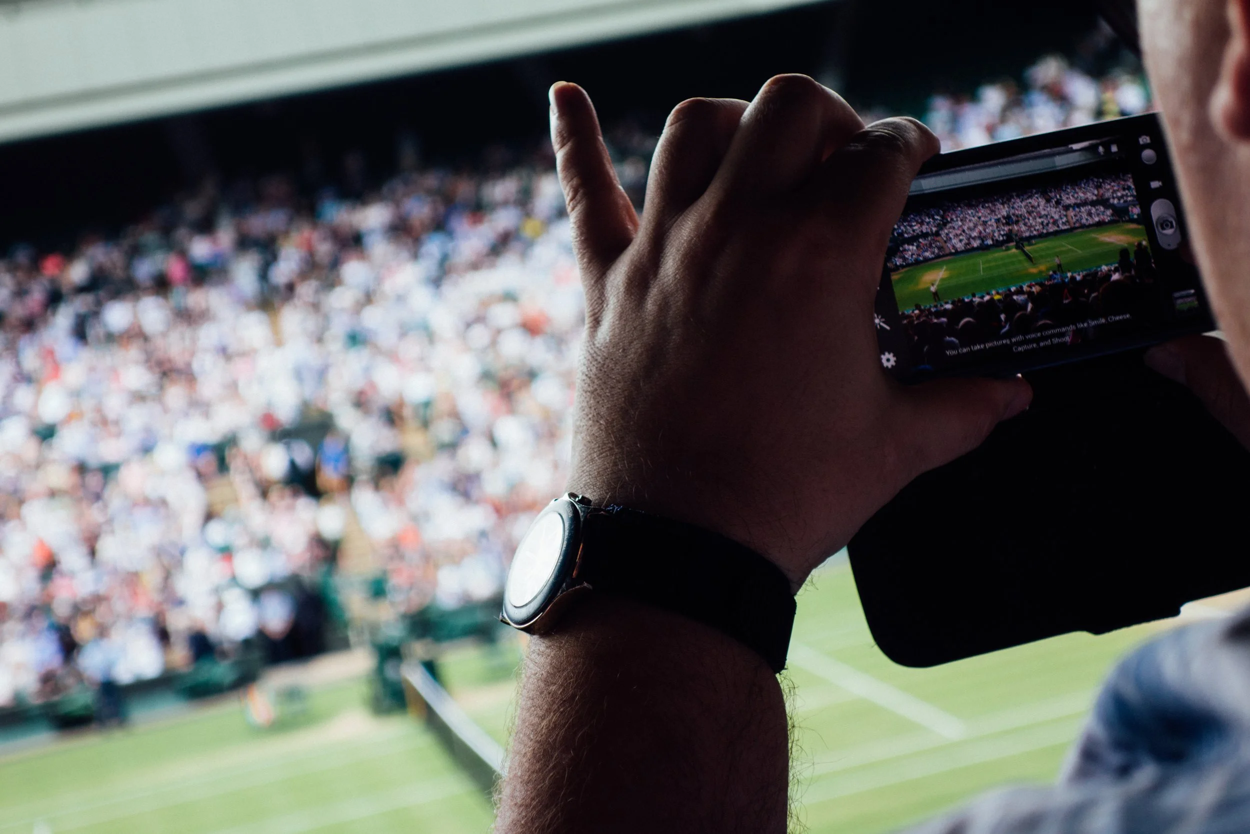 Person taking a photo of a Wimbledon Championships Centre Court.