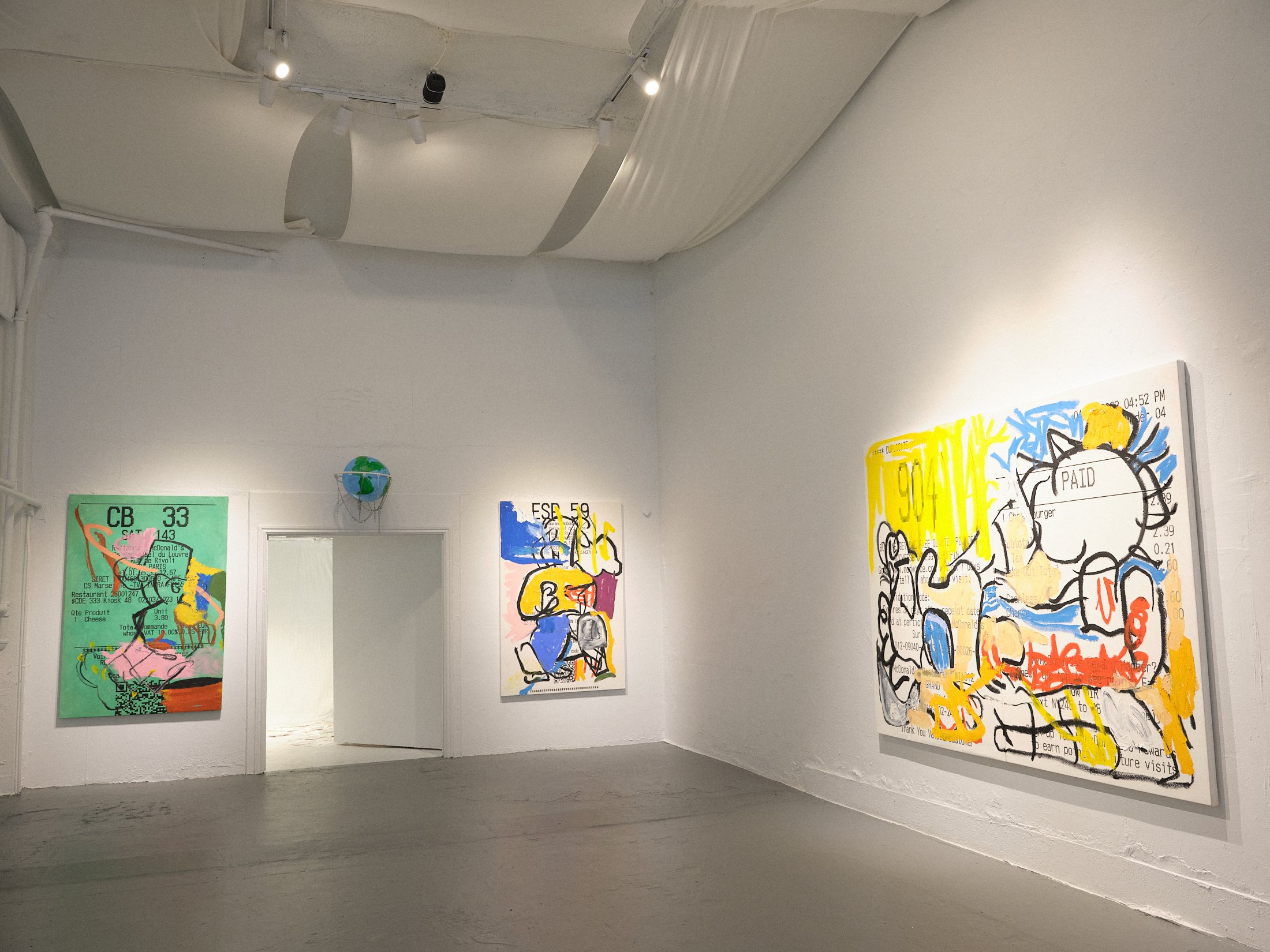 Gallery interior with three abstract paintings on white walls, featuring vibrant colors and text elements. Overhead lighting highlights the art. The space is minimalistic with a gray floor and a partial open door.