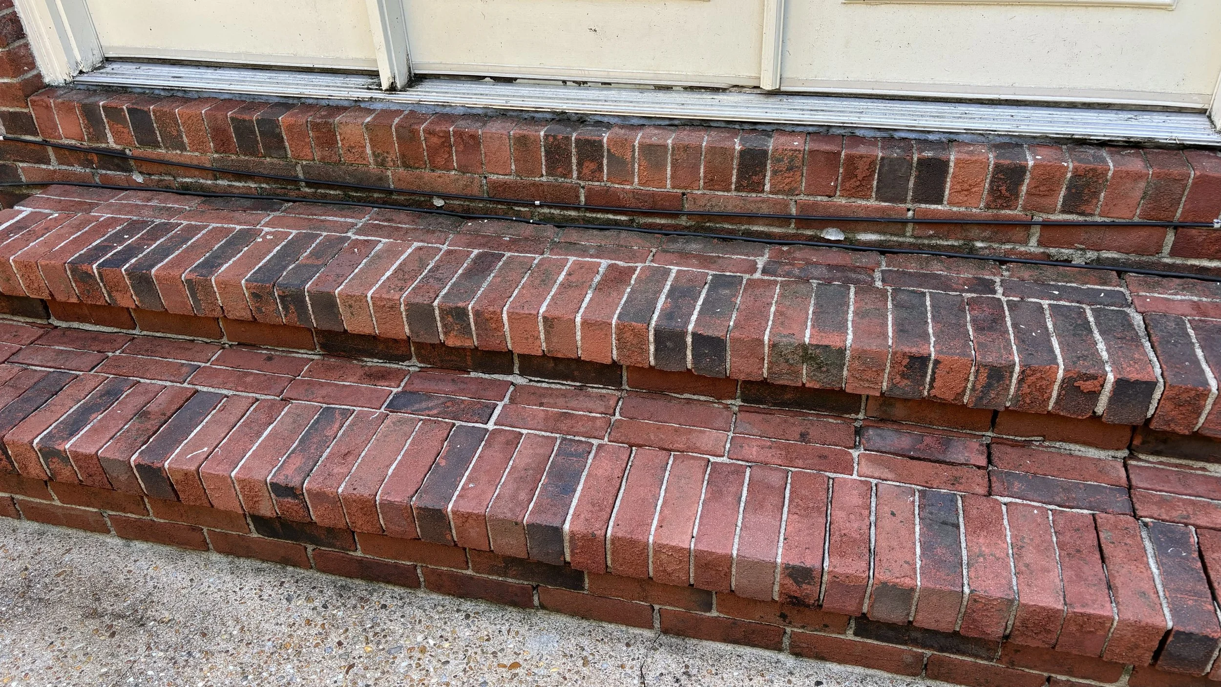 Red brick steps leading up to a doorway with visible wear and a cable running along the second step.