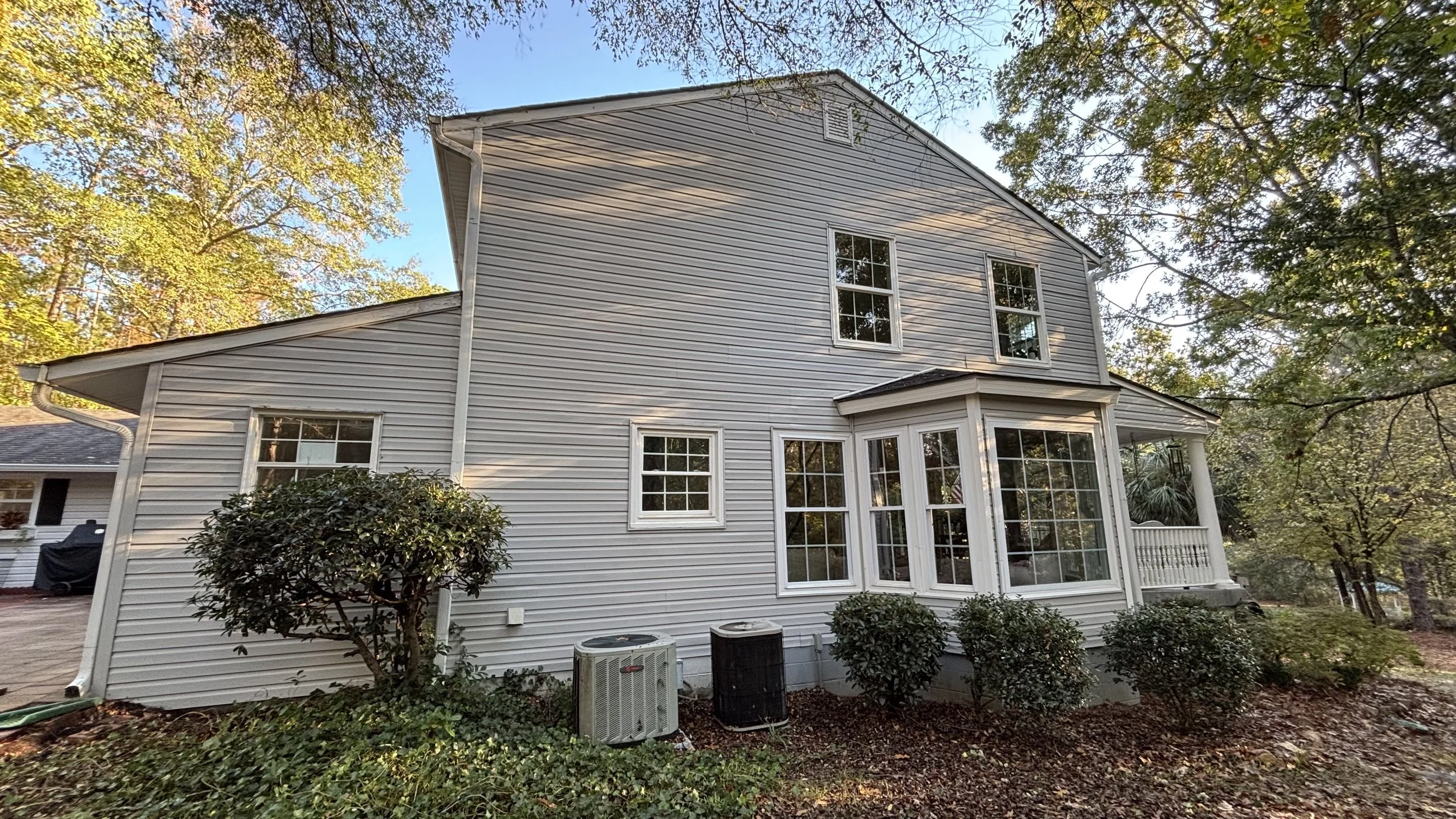 Gray house exterior with large windows, surrounding trees, and air conditioning units.
