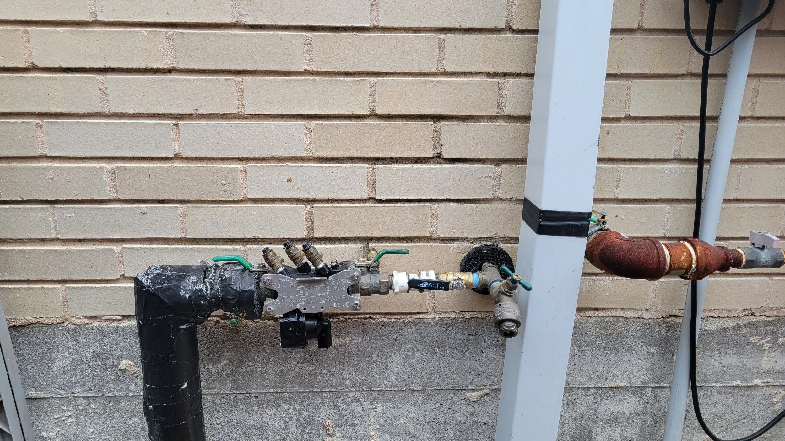 Central Texas pool backflow preventer on the side of beige brick house.
