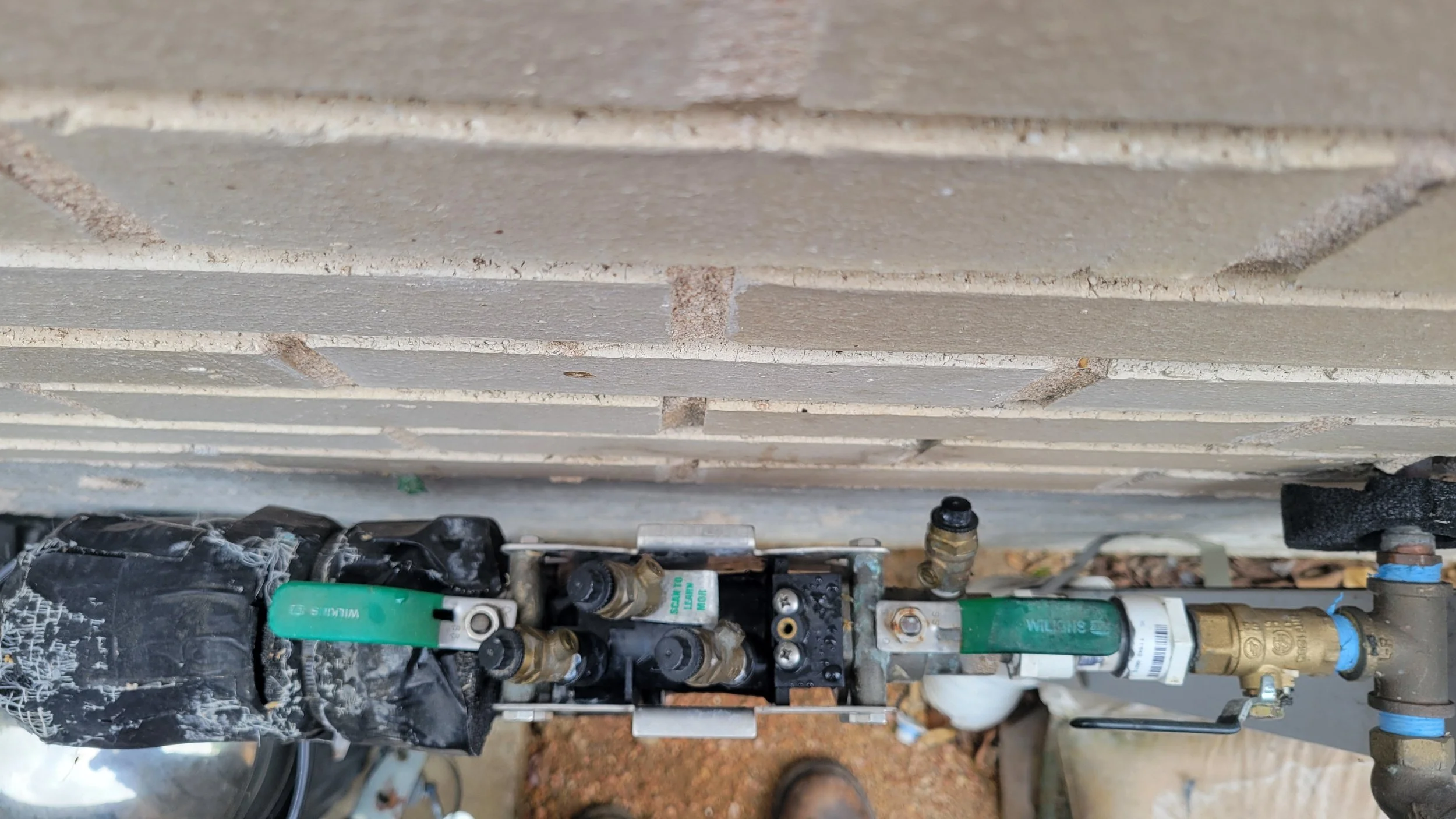 Close-up of outdoor wall mounted backflow preventer on the side of a beige brick house