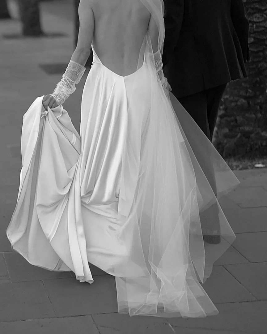 A woman in a wedding dress holding the bottom of her gown, walking next to a man in formal attire.