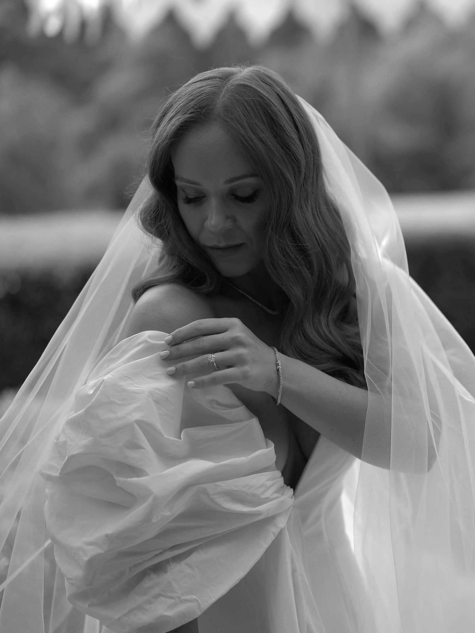 Graceful bride adjusting her voluminous sleeve beneath a flowing veil, captured in soft light to highlight the elegance and emotional stillness of her wedding morning.
