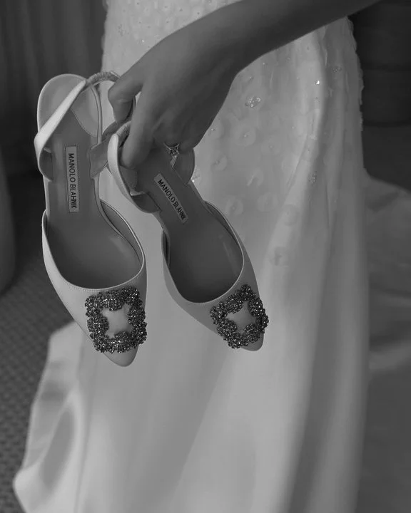 Bride holding embellished Manolo Blahnik heels against her gown, showcasing refined bridal details and luxurious wedding styling.