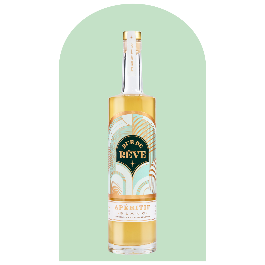 A bottle of Rue de Rêve Aperitif Blanc with a gold cap and pastel-colored label against a mint green background.