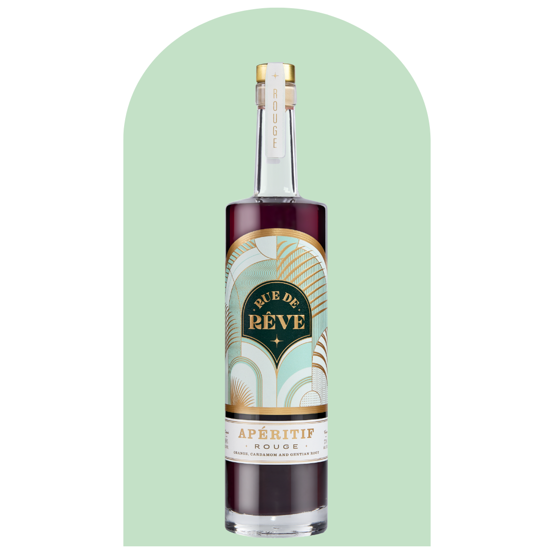 Bottle of Rue de Rêve Aperitif Rouge, with a gold and black label, on a light green background.