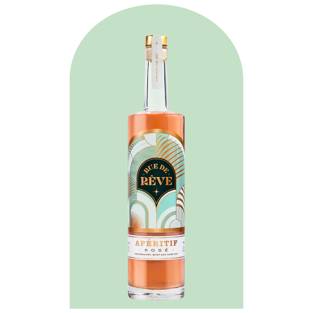 A tall glass bottle of Rue de Rêve Aperitif Rosé with a gold cap, label featuring abstract pastel-colored designs, set against a mint green background with a rounded arch shape.