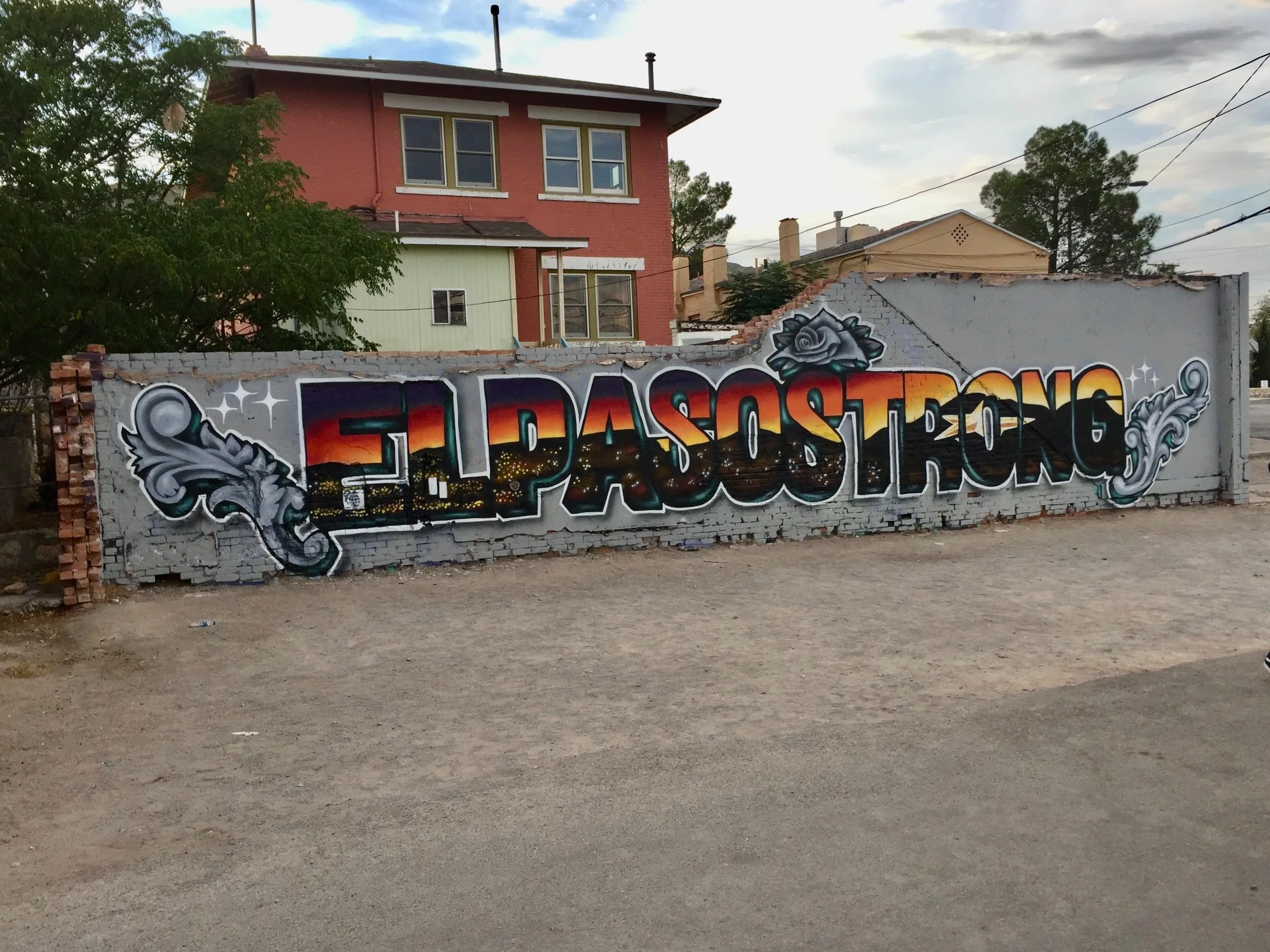 Mural with 'El Paso Strong' graffiti on a wall near a house.