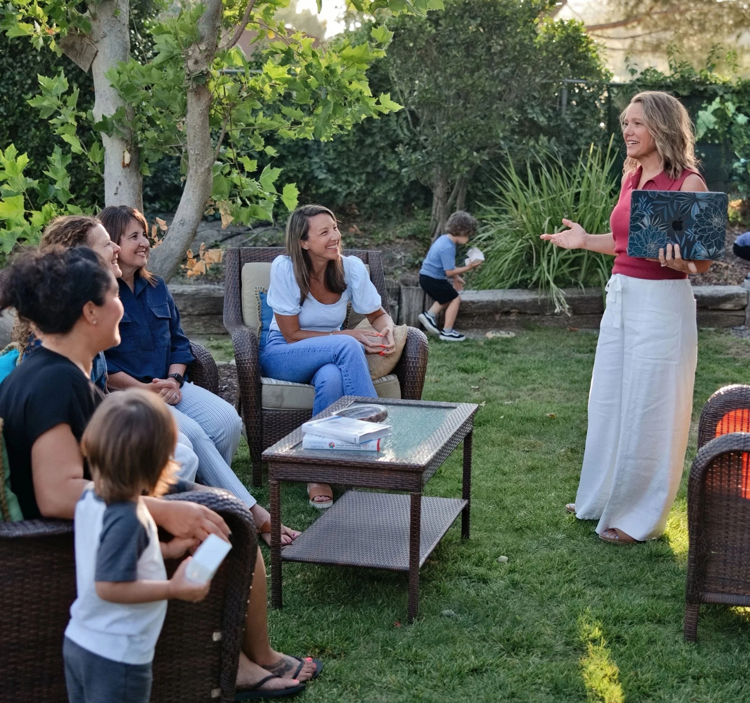 Whitney delivers a talk in front of a small group of women in the backyard while children play in the background