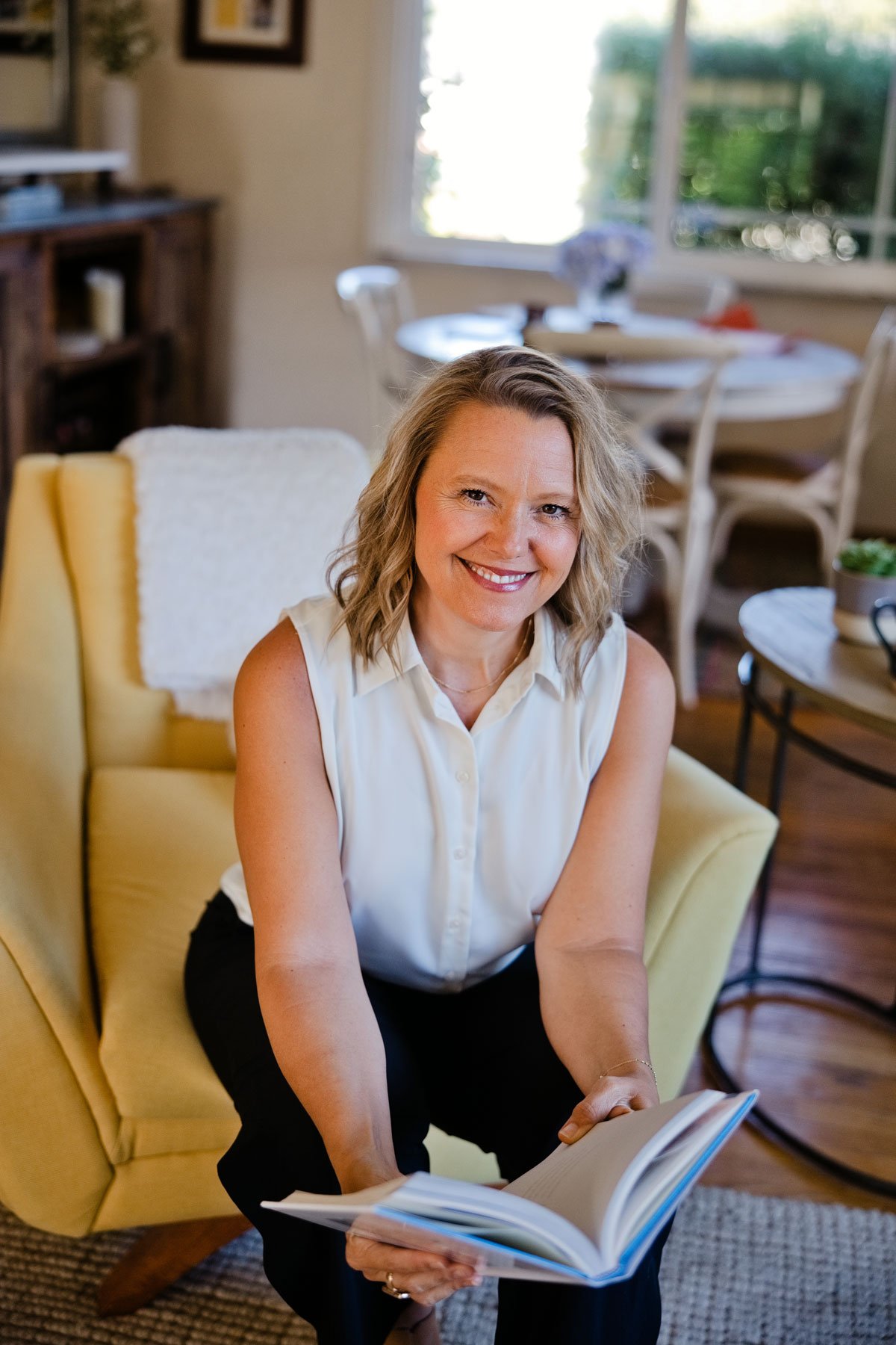 Whitney holds a book while sitting in a chair