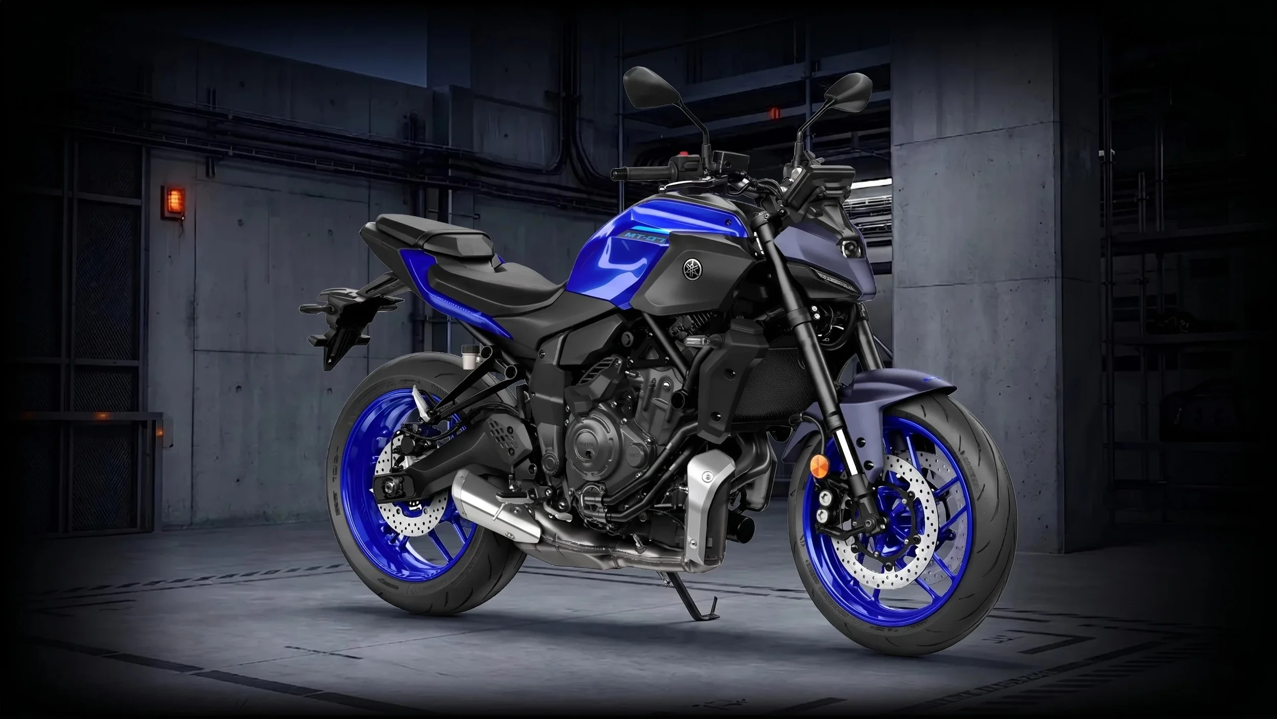 Une moto Yamaha bleue et noire dans un parking souterrain en béton, vue de côté.