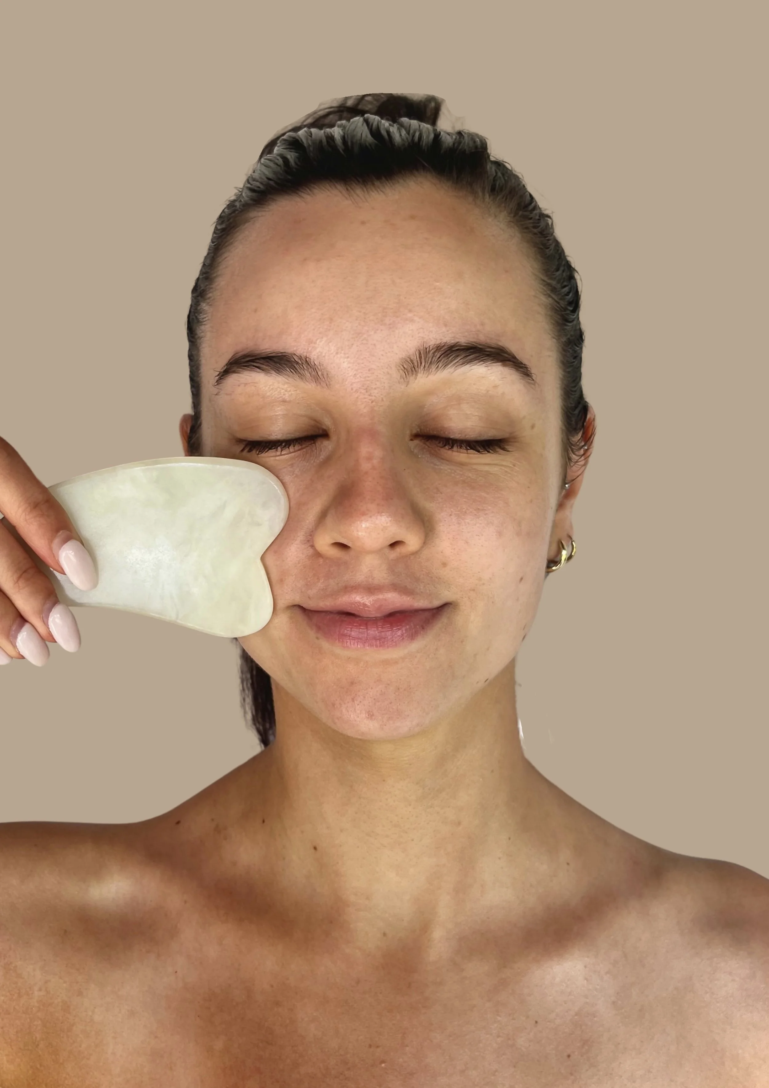 Person using a gua sha tool on their face with closed eyes.