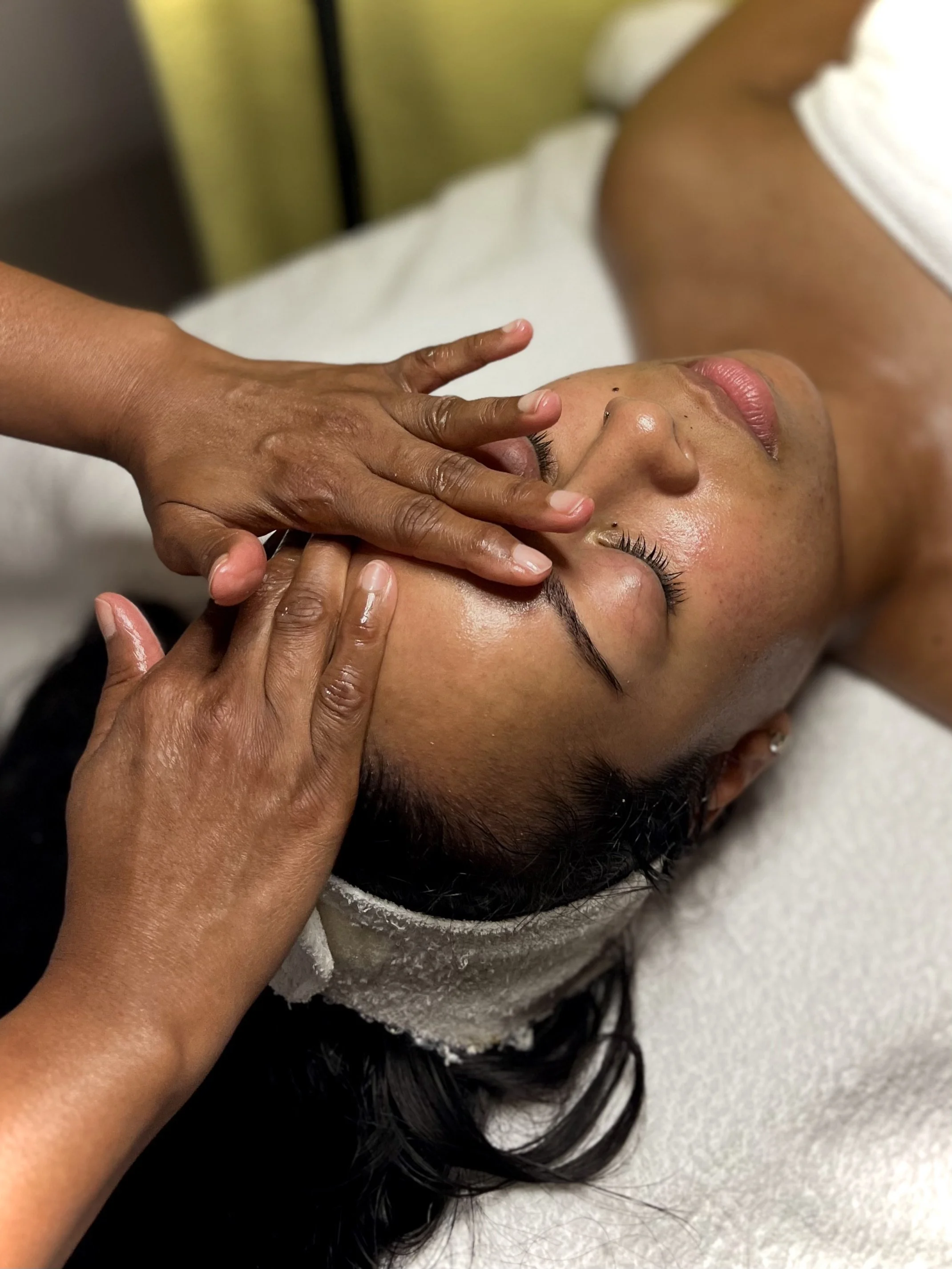 A person receiving a facial massage at a spa, with hands applying pressure on the forehead.