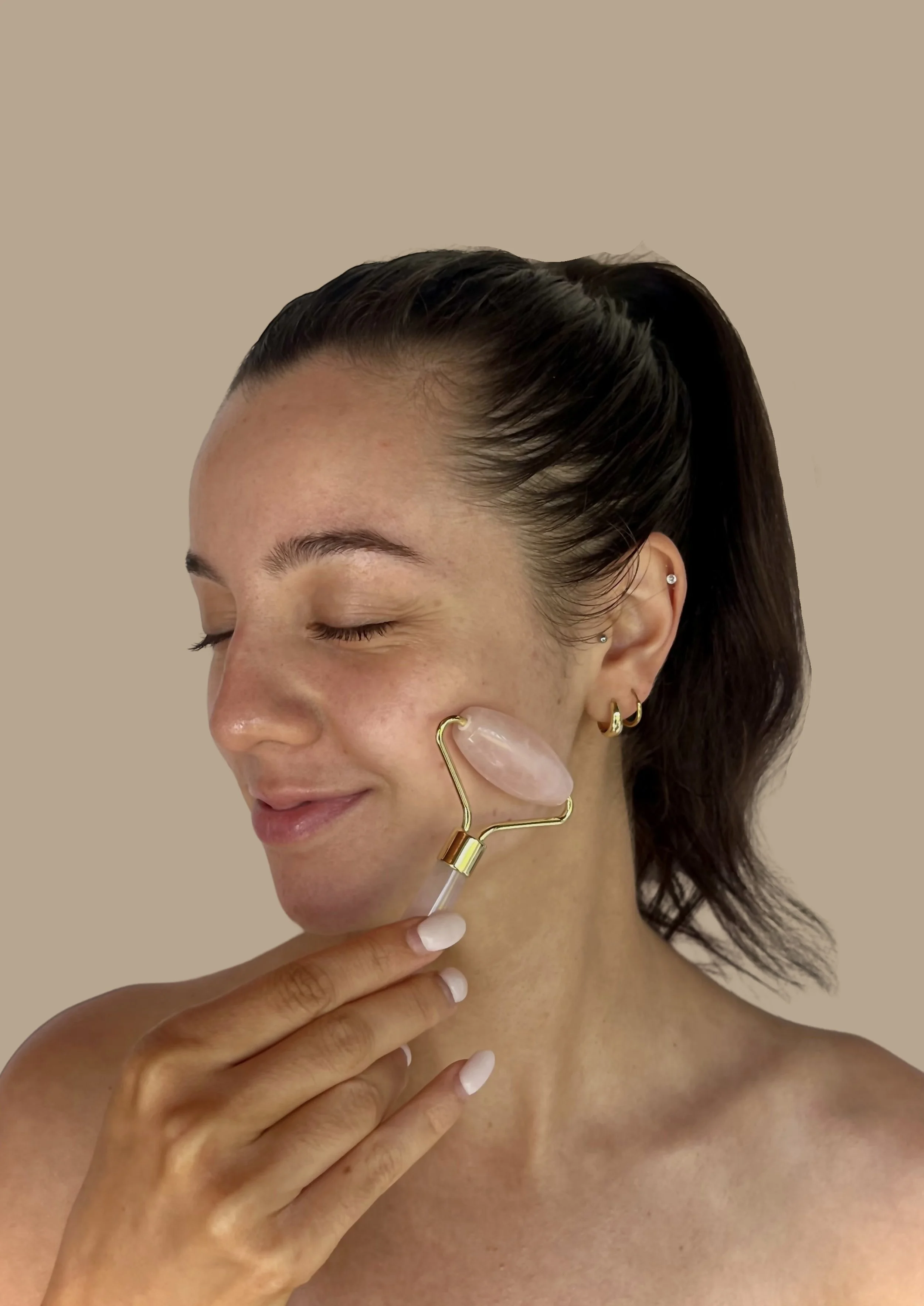 Woman using a pink jade roller on her face with a neutral background.