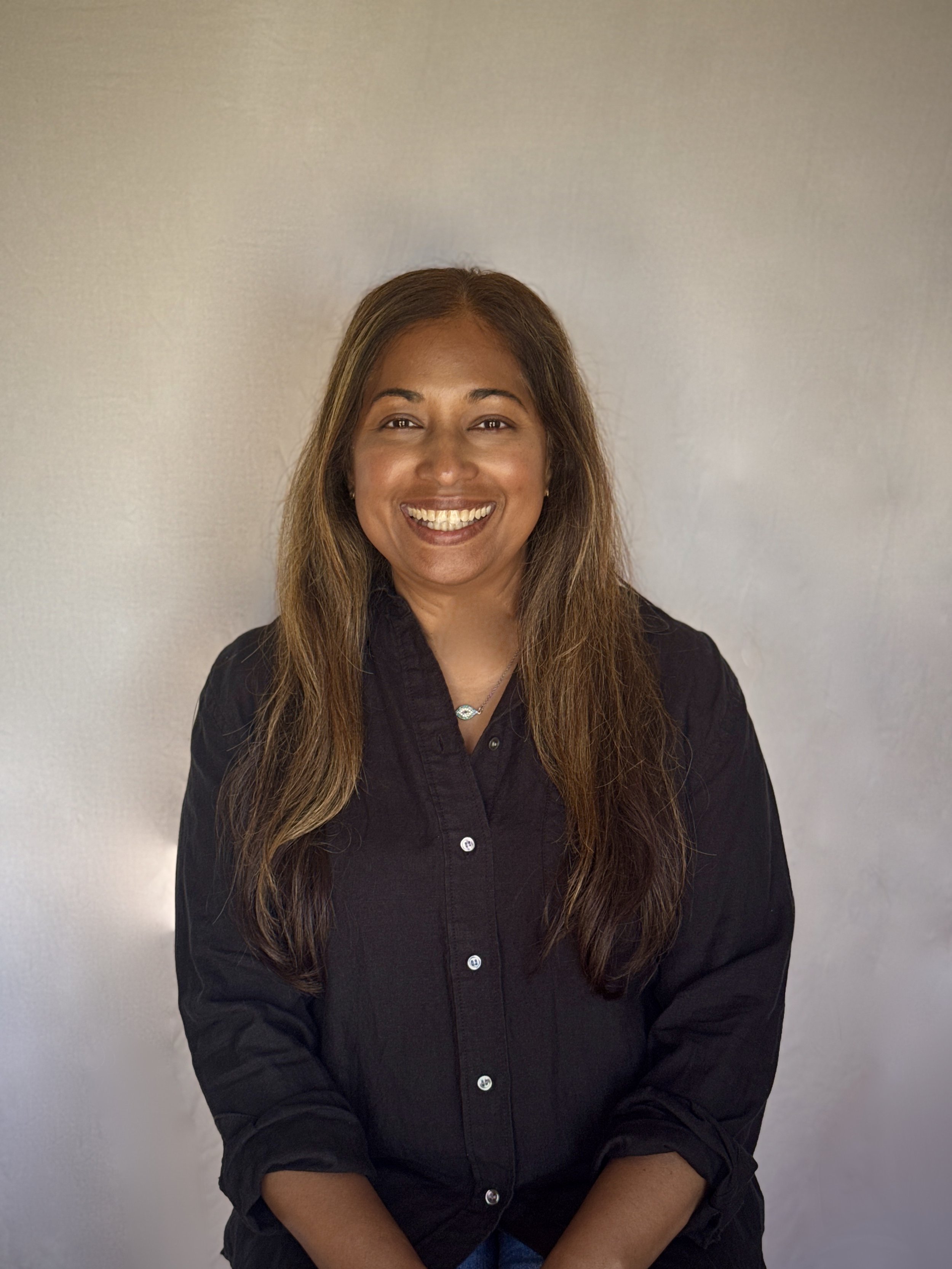 Smiling woman with long hair wearing a black button-up shirt against a neutral background.