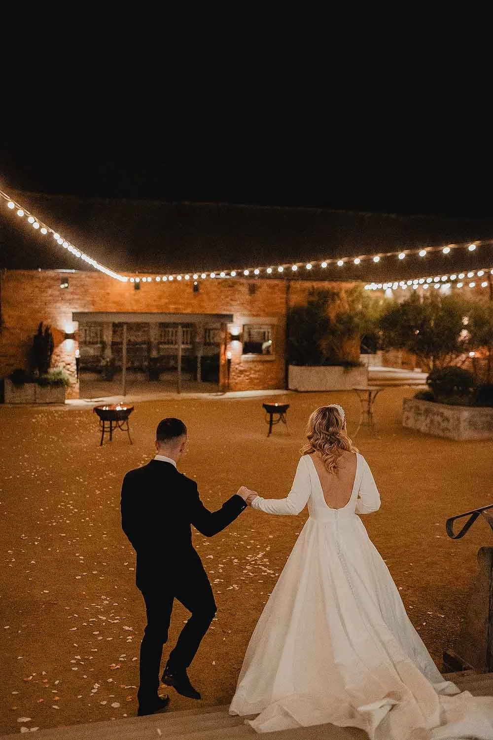 bride and groom holding hands in a wedding venue at night with lights