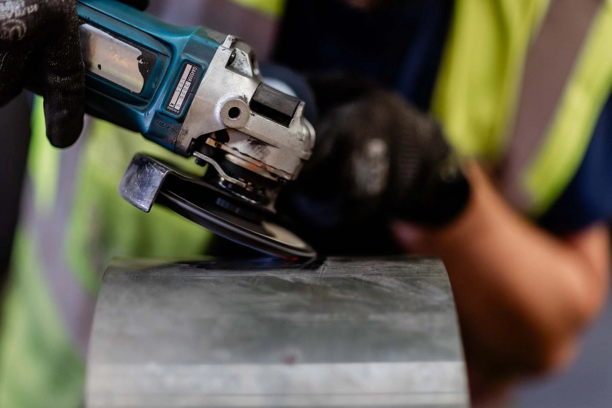Close-up of a power drill being used on a metal surface by a person wearing black gloves.