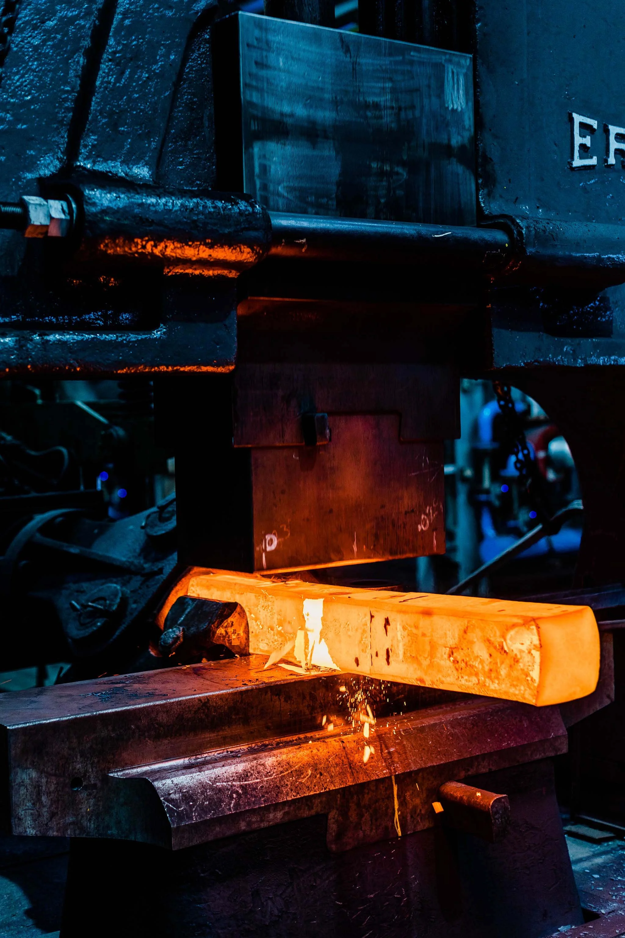 A piece of steel is being heated in a blacksmith forge, glowing orange from the heat, with sparks flying off as it is being worked on.