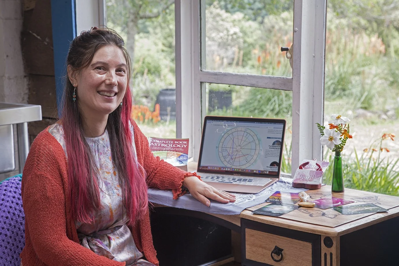 Women with long red hair doing astrology readings with nature outside the window, spiritual guidance for meaning, clarity and transformation.
