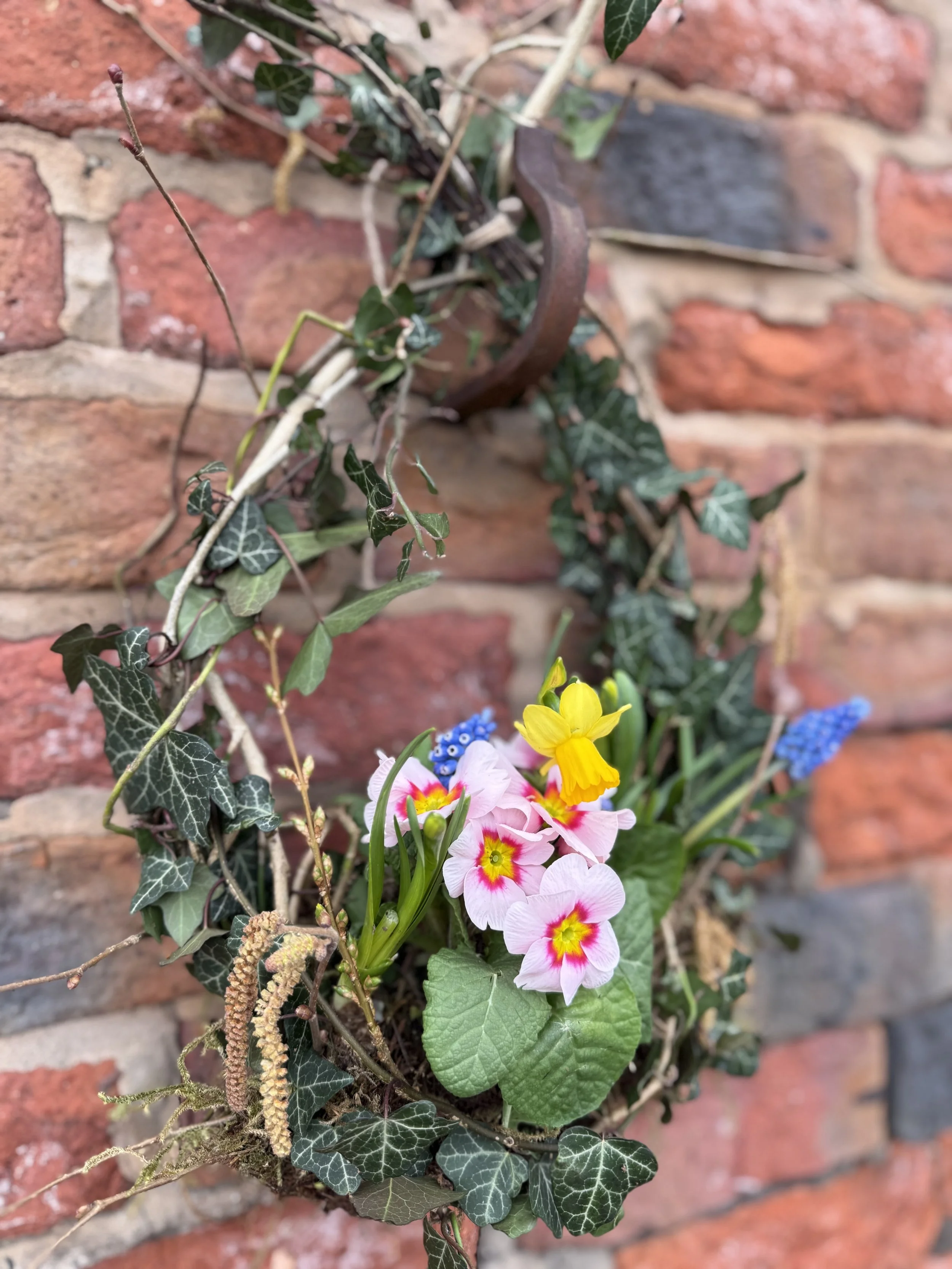 Living spring wreath made with fresh greenery and seasonal plants, arranged on a natural base.